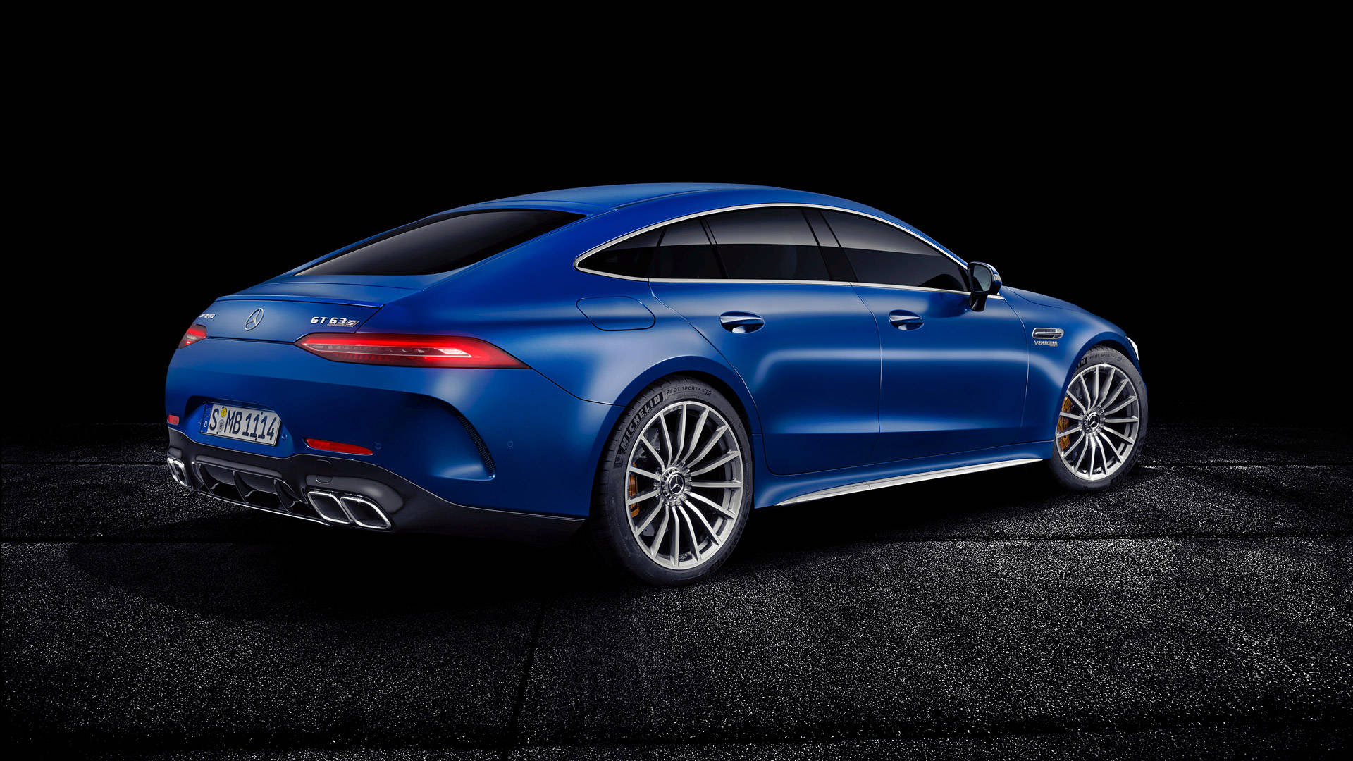 梅賽德斯-AMG GT 63 壁紙 — 一輛時尚的藍色 Mercedes-AMG GT S 轎跑車在黑色瀝青背景下於攝影棚燈光下閃耀。