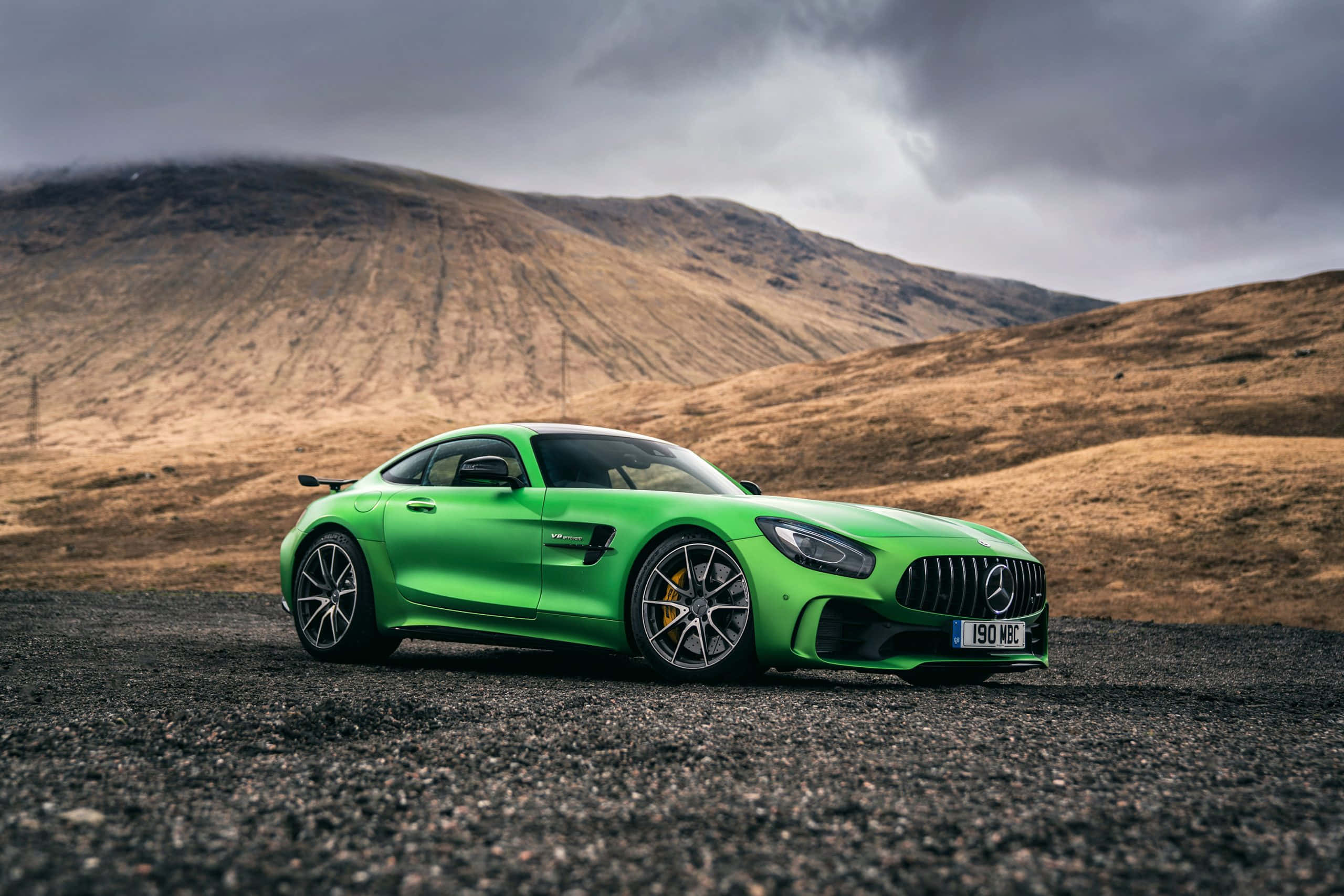 梅賽德斯-AMG GT R 配棕色山坡背景 壁紙 — 一輛鮮綠色平治AMG GT跑車停在碎石上，背景是戲劇性的多雲天空和荒蕪的山丘。