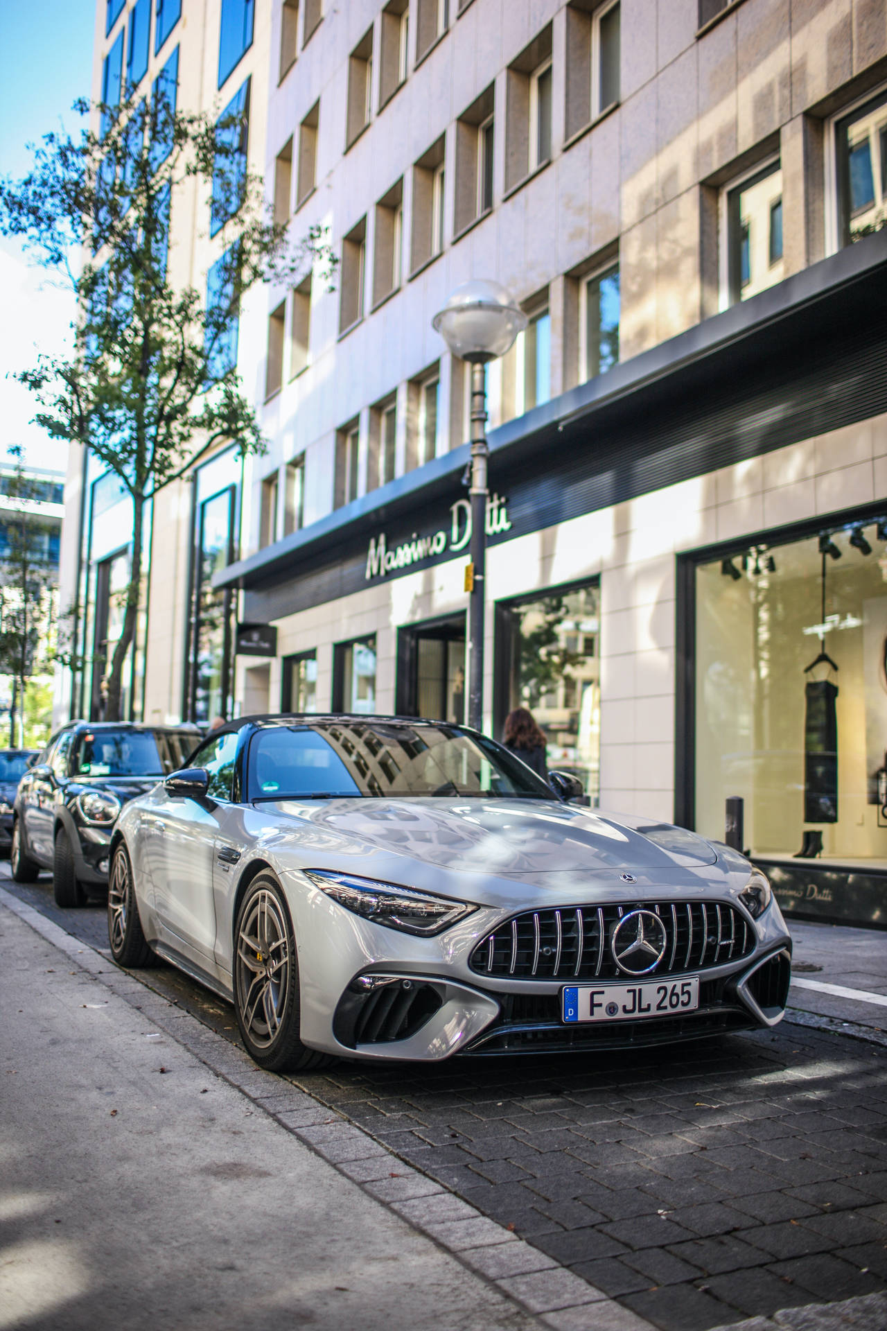 銀色 Mercedes-AMG GT 停泊在陽光明媚的城市街道上，旁邊是一家豪華精品店。