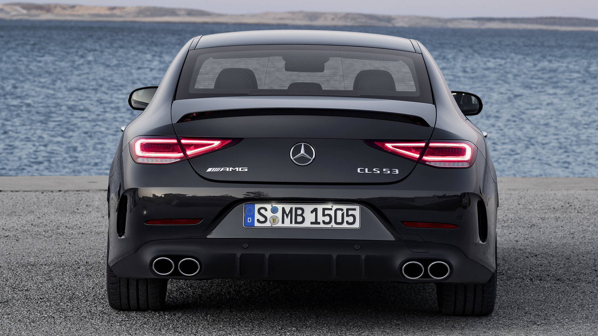 梅賽德斯-AMG 熱紅尾燈 壁紙 — 一架時尚黑色Mercedes-AMG CLS 53停在灰色路面上，背後是平靜的藍色大海。