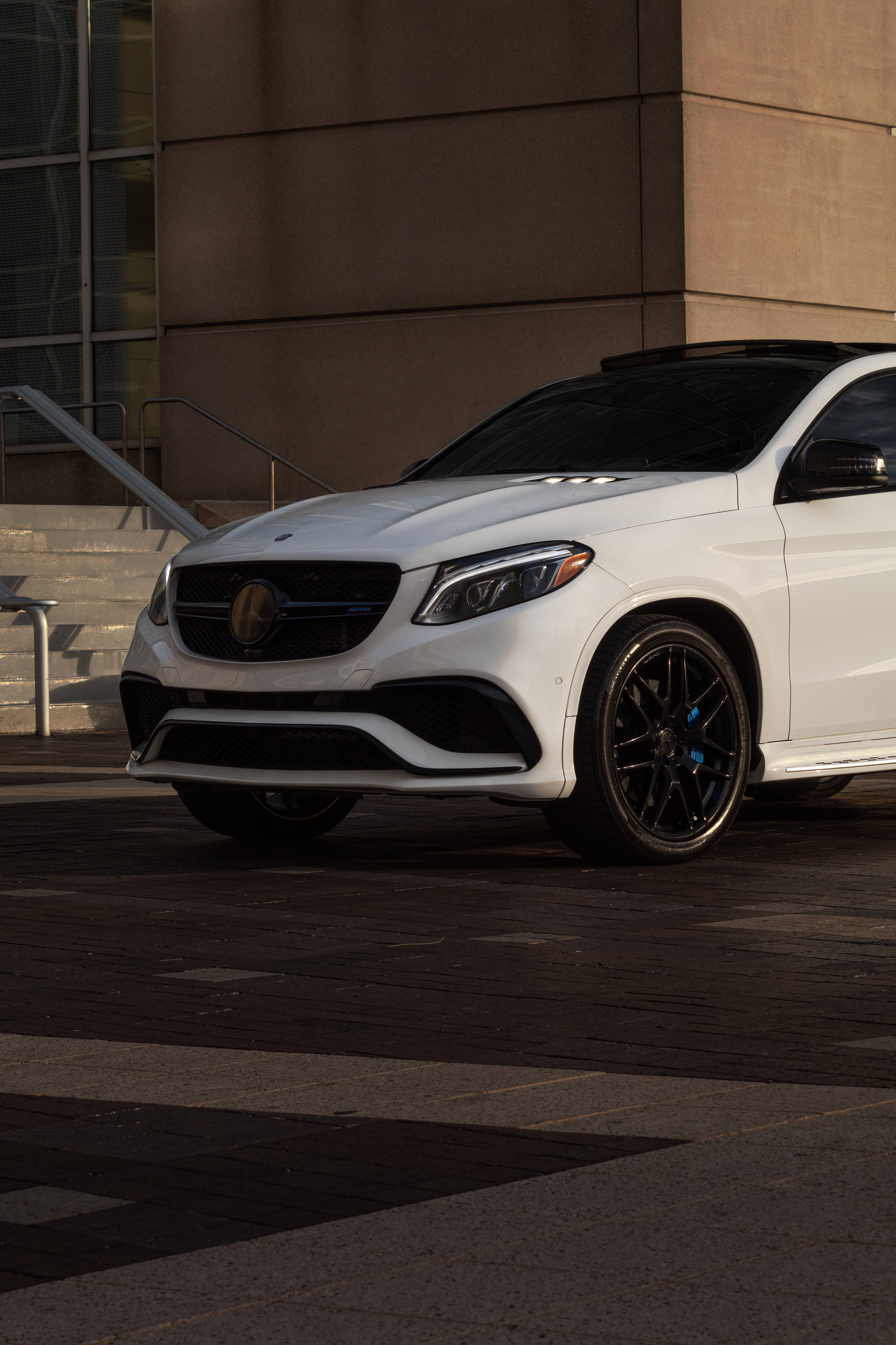 梅賽德斯-AMG 白色塗裝車款 壁紙 — 一架時尚的白色Mercedes-AMG GLE63 SUV停泊在陽光普照的城市行人路上，旁邊是一座現代建築。