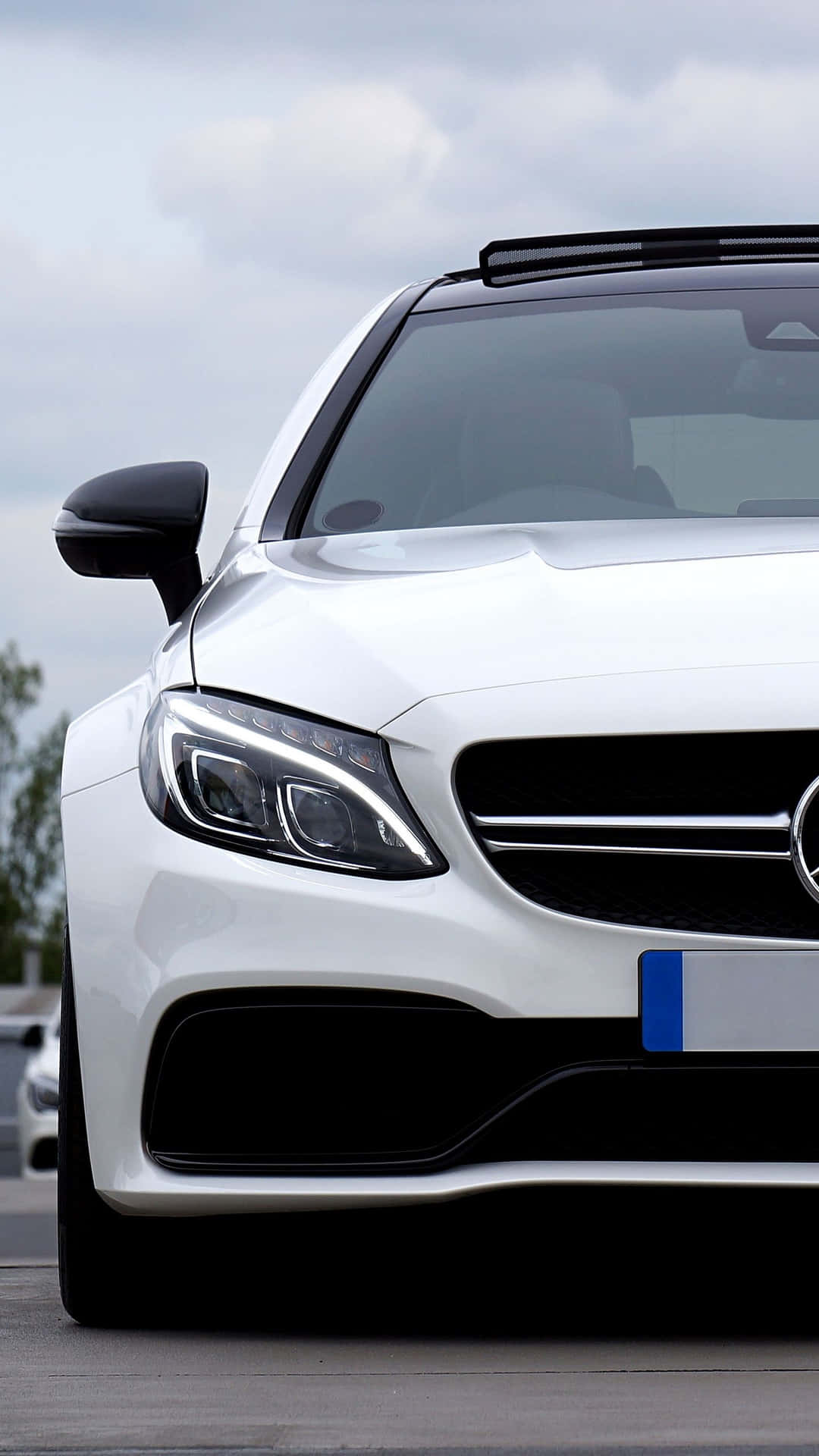 白色 Mercedes-Benz 汽車，帶有黑色飾邊和現代車頭燈，停放在戶外。