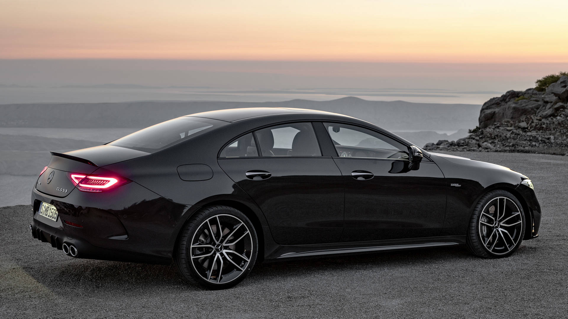 梅賽德斯-AMG 細膩黑色車身 壁紙 — 一架時尚的黑色 Mercedes-AMG CLS450 轎跑車停在日落時分的海岸懸崖上，尾燈閃閃發光。