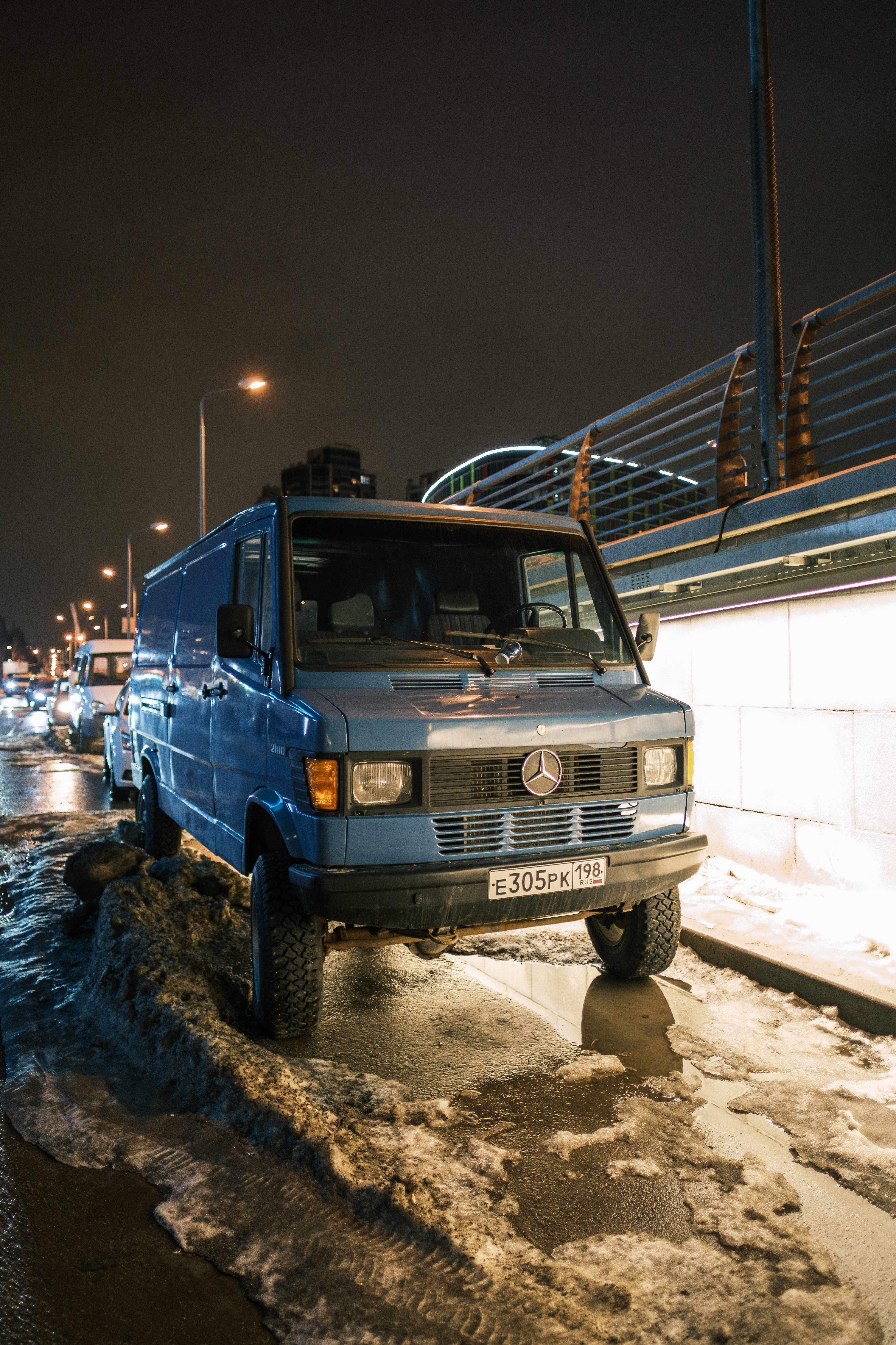 梅賽德斯-AMG 貨車 壁紙 — 一輛藍色 Mercedes-Benz 客貨車在夜間停泊在積雪的市區街道上，街燈在濕雪上投射出倒影。