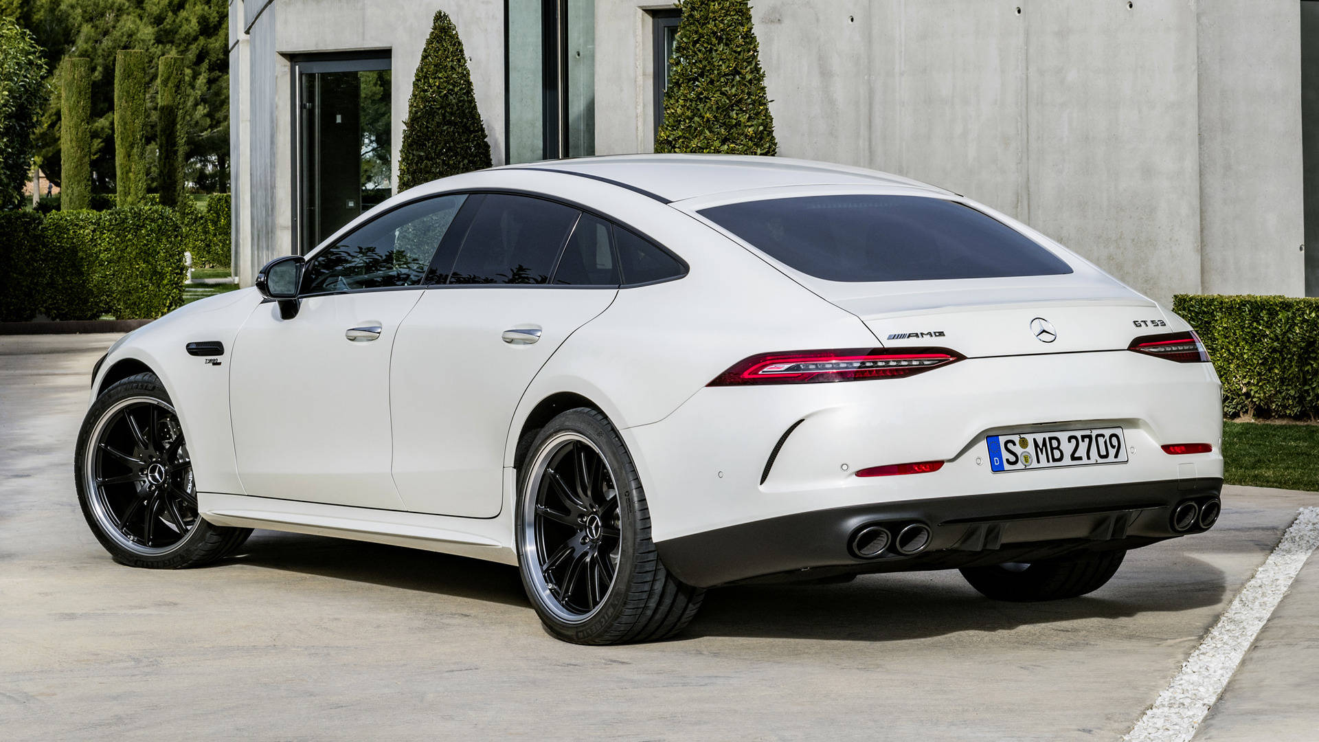 梅賽德斯-AMG 車型 壁紙 — 一架時尚的白色梅賽德斯-AMG GT 63 S 停泊在混凝土車道上，旁邊是帶有修剪整齊樹籬的現代建築。