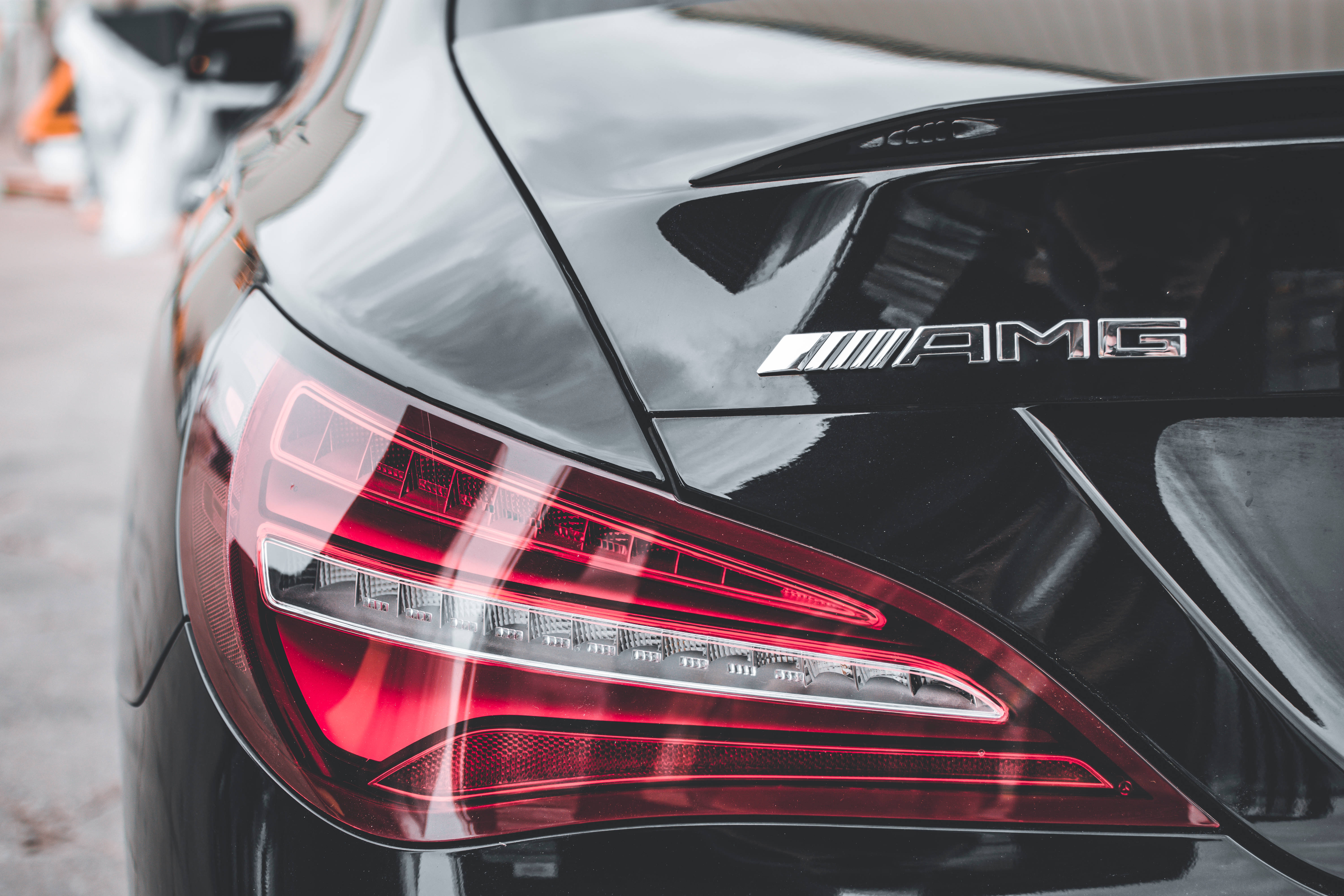 梅賽德斯-AMG 銀色字樣徽章 壁紙 — 黑色AMG汽車後方特寫，配備發光紅色尾燈和鍍鉻標誌。