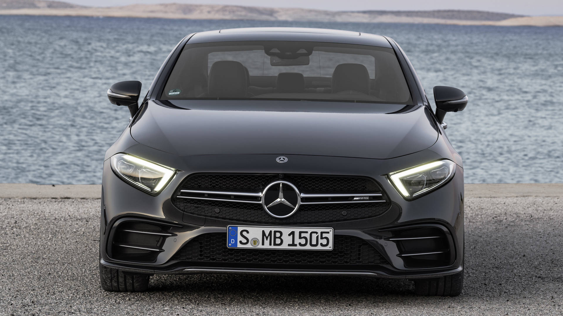 梅賽德斯-AMG 銀色徽章標誌 壁紙 — 一架型格黑色Mercedes-AMG A45停泊在海濱道路上，背景有海浪。