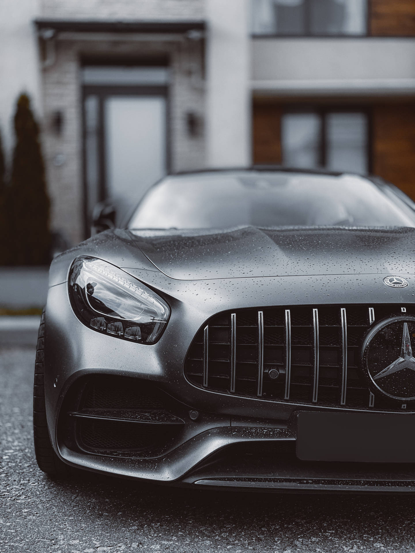 啞光黑色Mercedes-AMG跑車帶有雨滴，停在一棟現代房屋前。