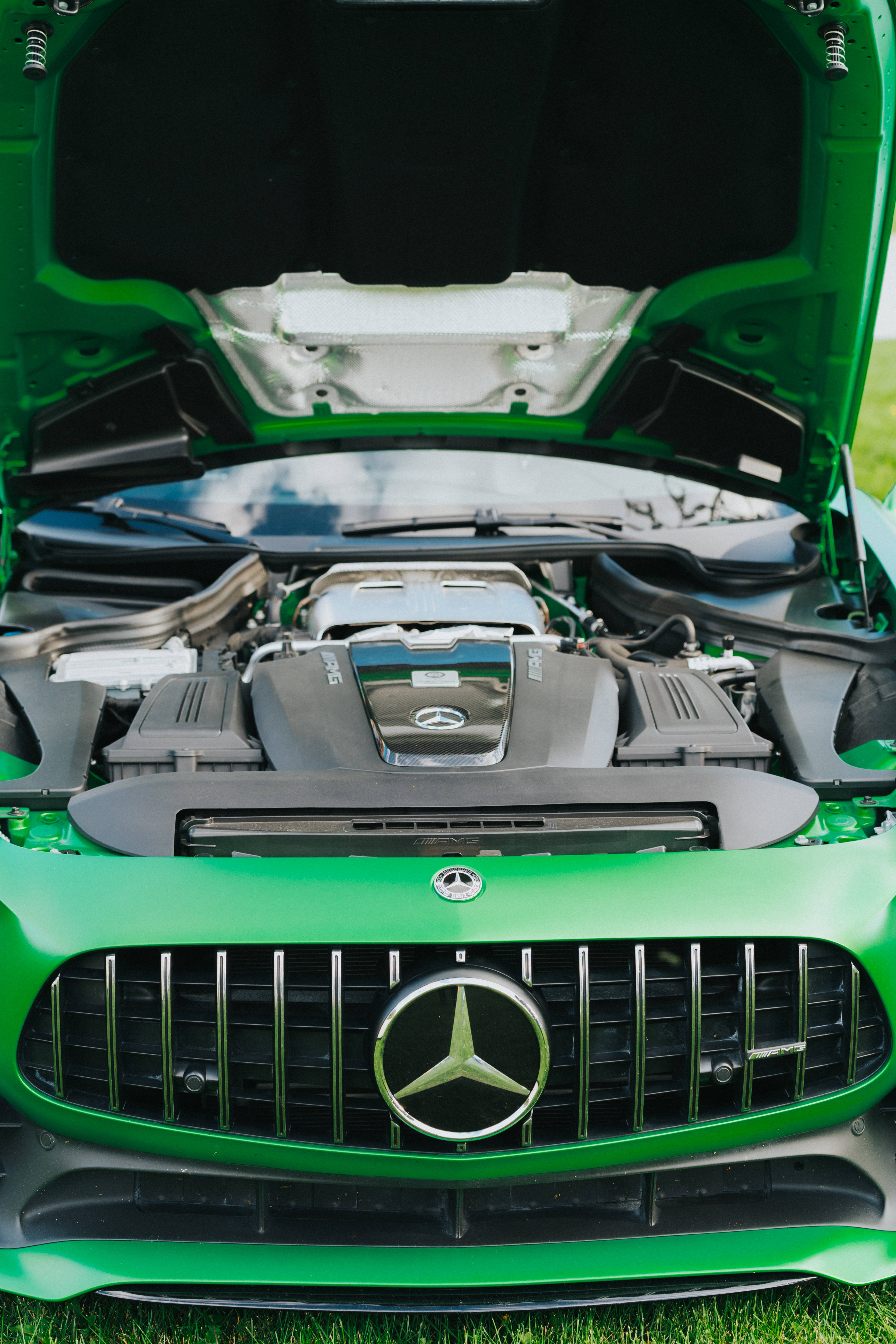 梅賽德斯-AMG 雙引擎 壁紙 — 一輛充滿活力的綠色Mercedes-AMG跑車，引擎蓋打開，露出強勁的引擎，停在草地上。