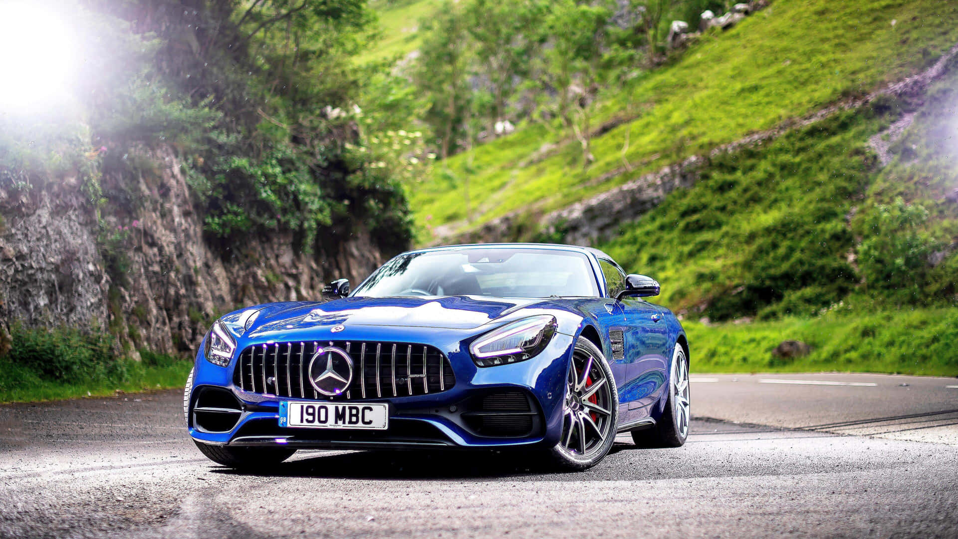 藍色 Mercedes-AMG GT 跑車在蜿蜒的山路上，周圍有綠色山丘。