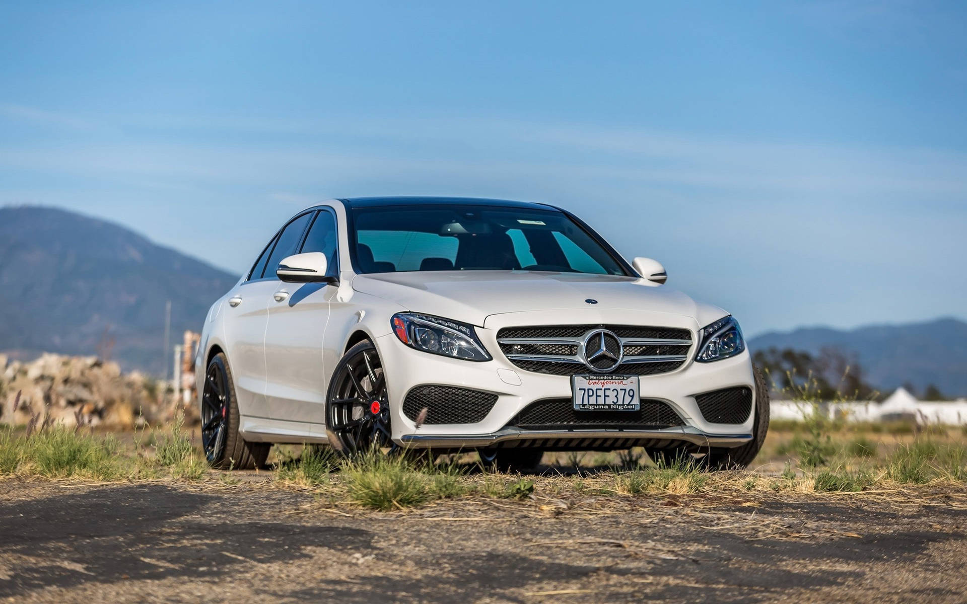 陽光明媚的日子裡，白色Mercedes-AMG C63停泊在靠近山脈的碎石路上。