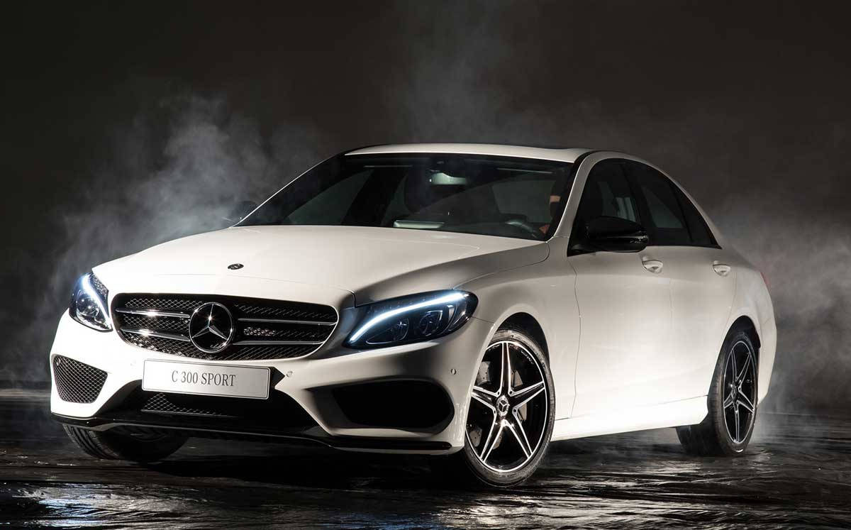 梅賽德斯-奔馳 C300 珍珠白 壁紙 — 一輛時尚的白色 Mercedes C 300 Sport 轎車在戲劇性的攝影棚燈光下閃閃發光，煙霧在其激進的前格柵和發光的車頭燈周圍旋轉。