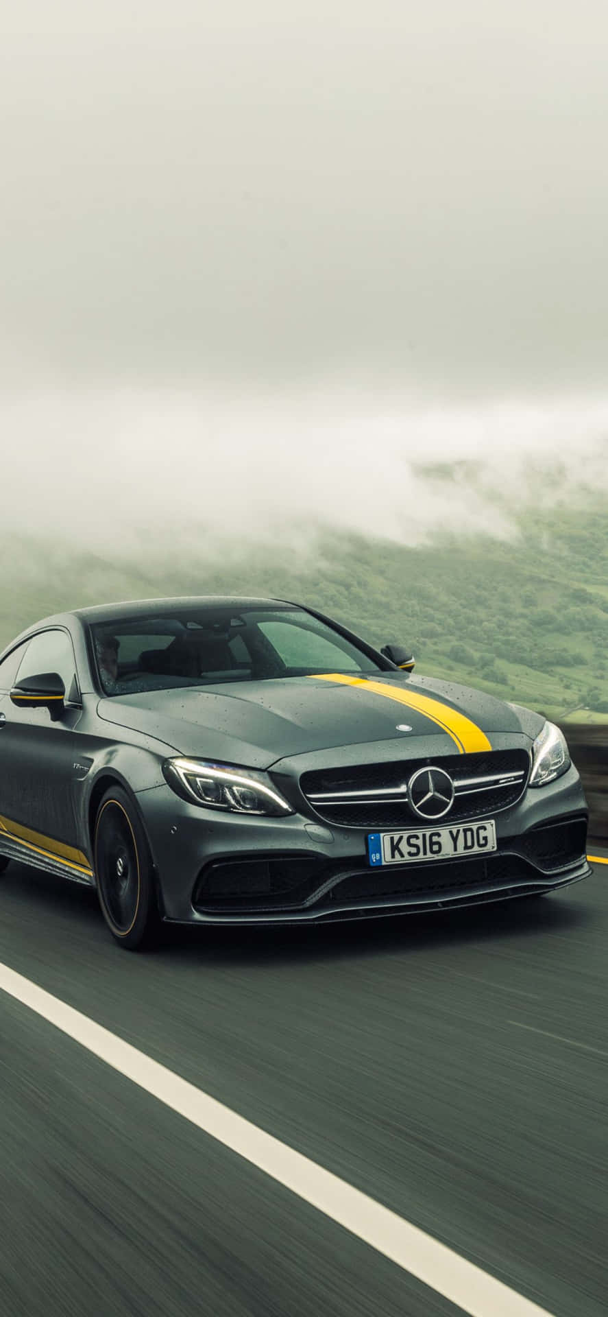 帶有黃色條紋的灰色 Mercedes-AMG 在霧氣瀰漫的山路上行駛。