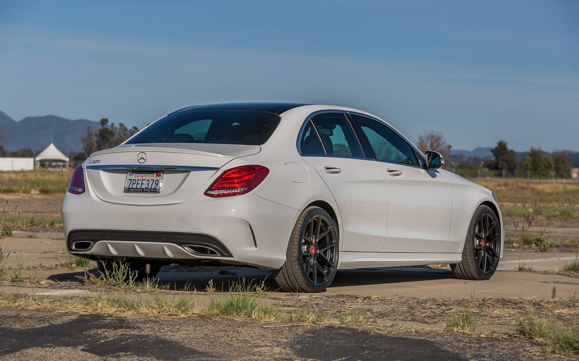 白色Mercedes C63 AMG轎車停在龜裂的柏油路上，背景有山脈。