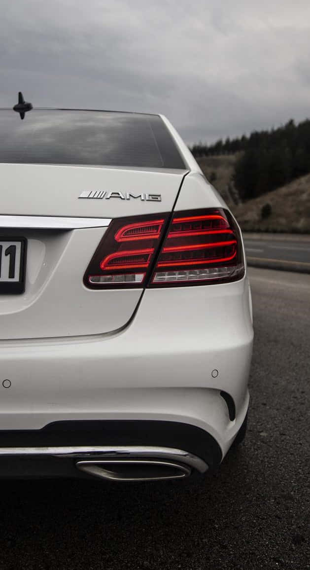 梅賽德斯-奔馳E級車尾燈特寫 壁紙 — 陰天時，白色 Mercedes-AMG 汽車後部及發光紅色尾燈的特寫。