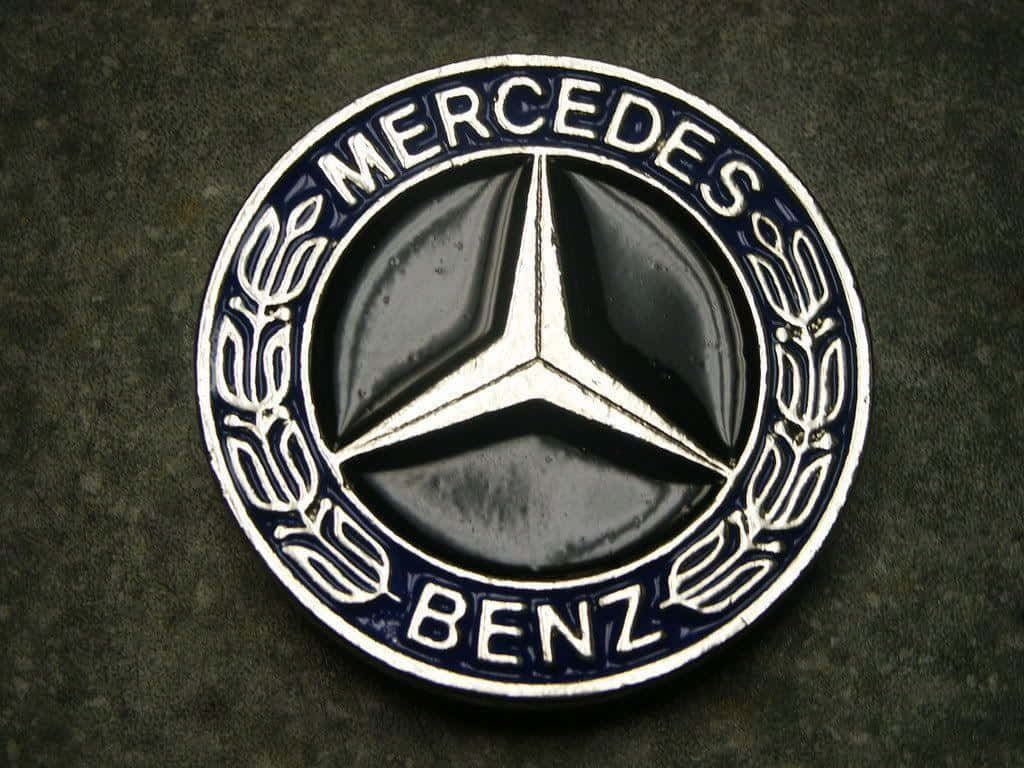 梅賽德斯-奔馳標誌 壁紙 — 經典 Mercedes-Benz 標誌的特寫，黑色背景上有一個銀色三叉星，周圍環繞著月桂花環和藍色琺瑯。