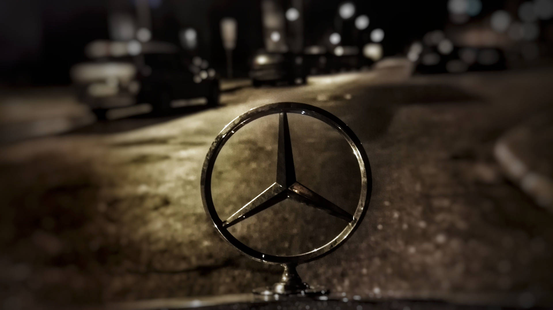 Mercedes-Benz 標誌在濕漉漉的人行道上，夜晚，後面有模糊的汽車。