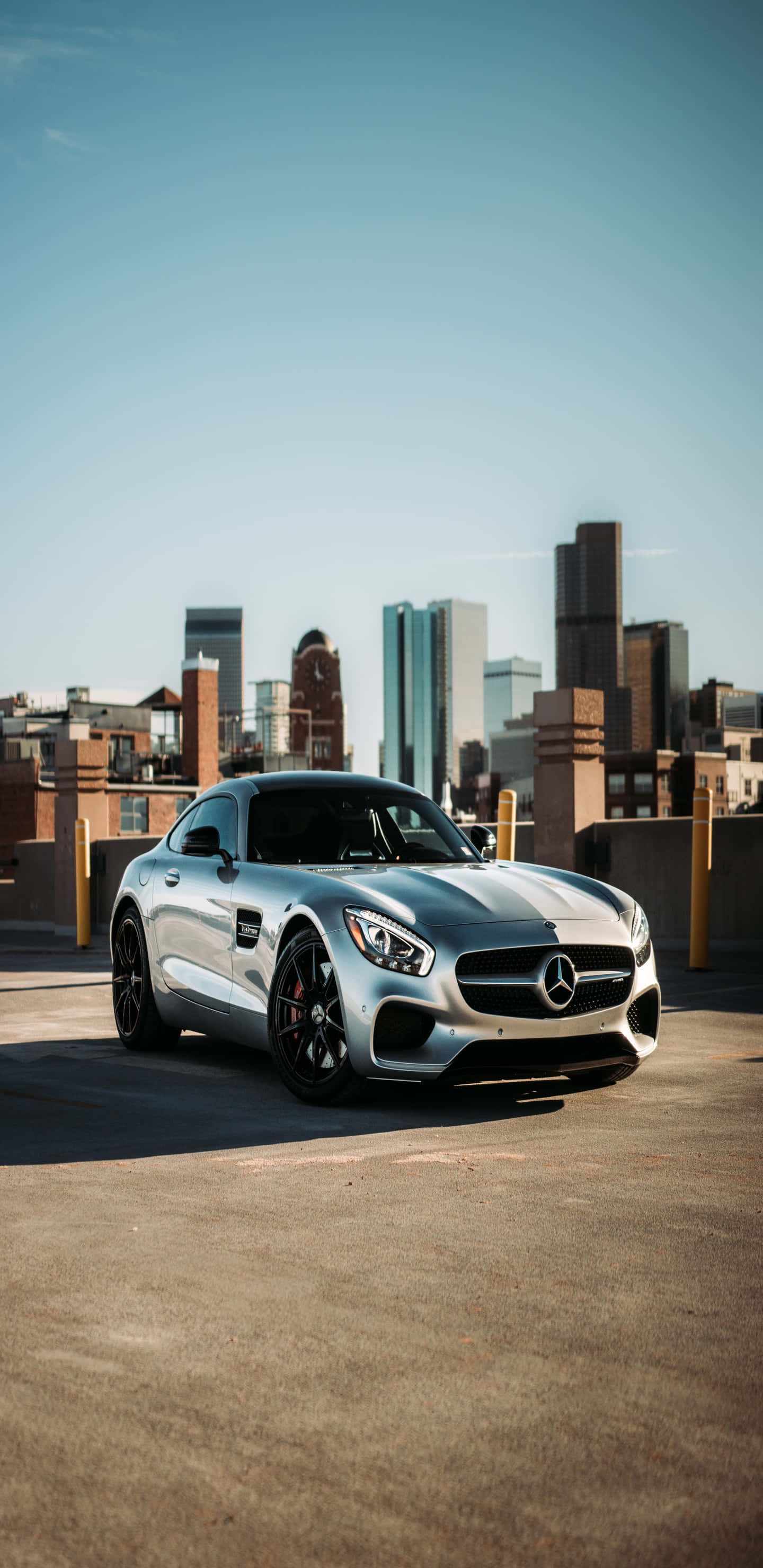 梅賽德斯-奔馳配城市建築背景 Pixel 3XL AMG GT-R 背景 壁紙 — 一架時尚的銀色 Mercedes-AMG GT 跑車停泊在屋頂上，背景是現代城市天際線和晴朗的藍天。