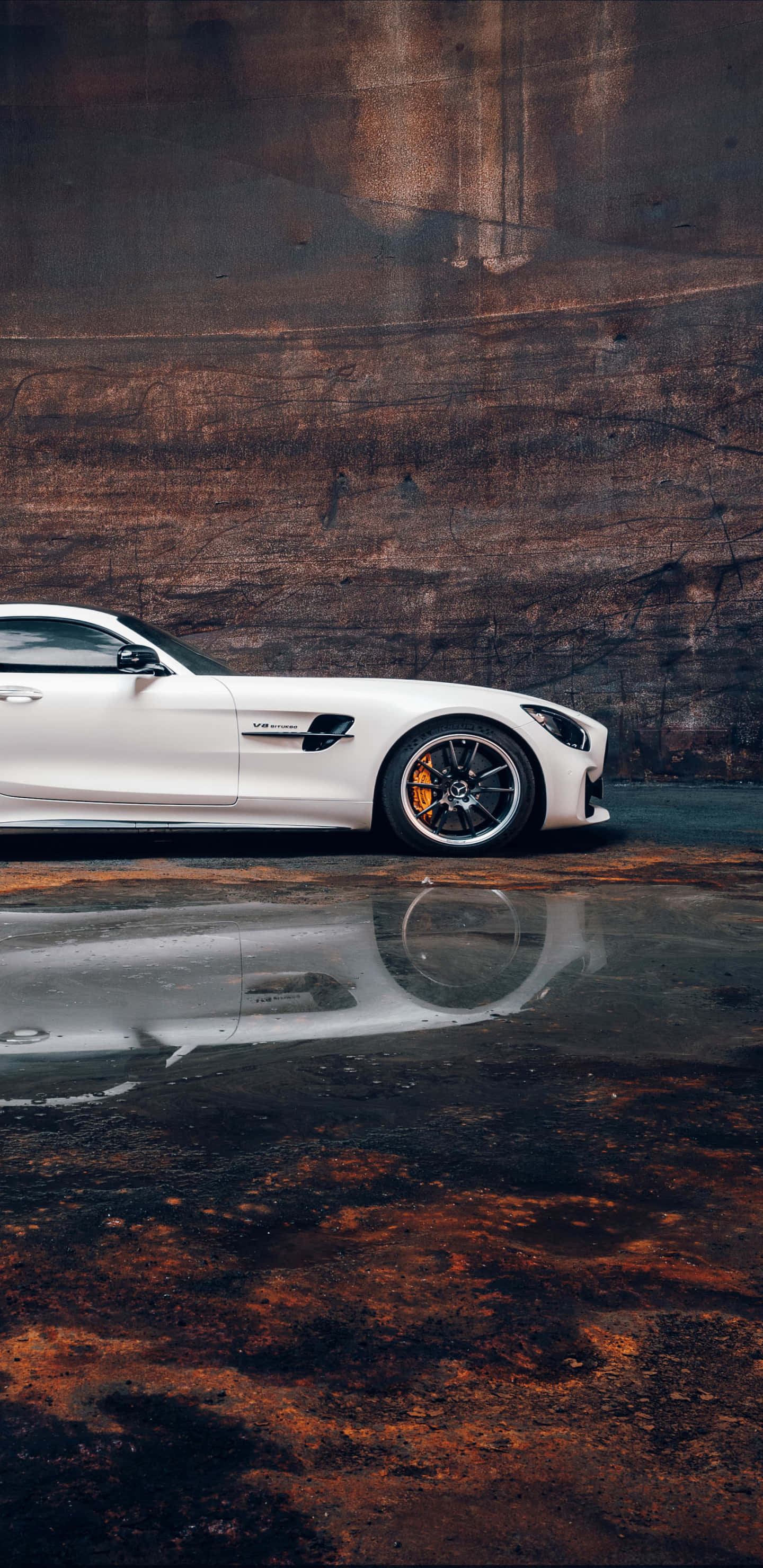 梅賽德斯-奔馳駛過濕地 Pixel 3XL AMG GT-R 背景 壁紙 — 一輛時尚的白色跑車在濕漉漉的路面上倒映，背景是質感粗糙的鏽牆。