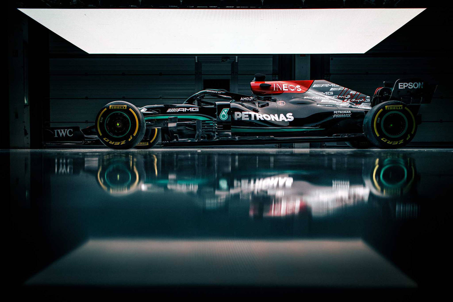 一輛帶有Petronas標誌的黑色和藍綠色一級方程式賽車，在黑暗車庫的光滑地板上反射。