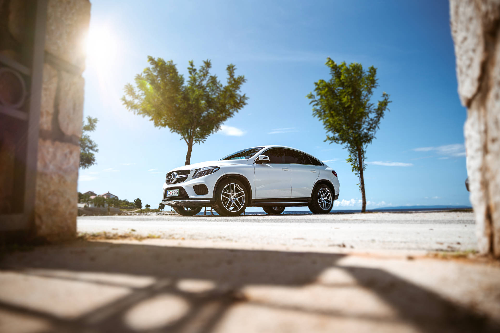 白色Mercedes-Benz SUV停泊在陽光明媚的海岸道路上，兩旁有石柱。
