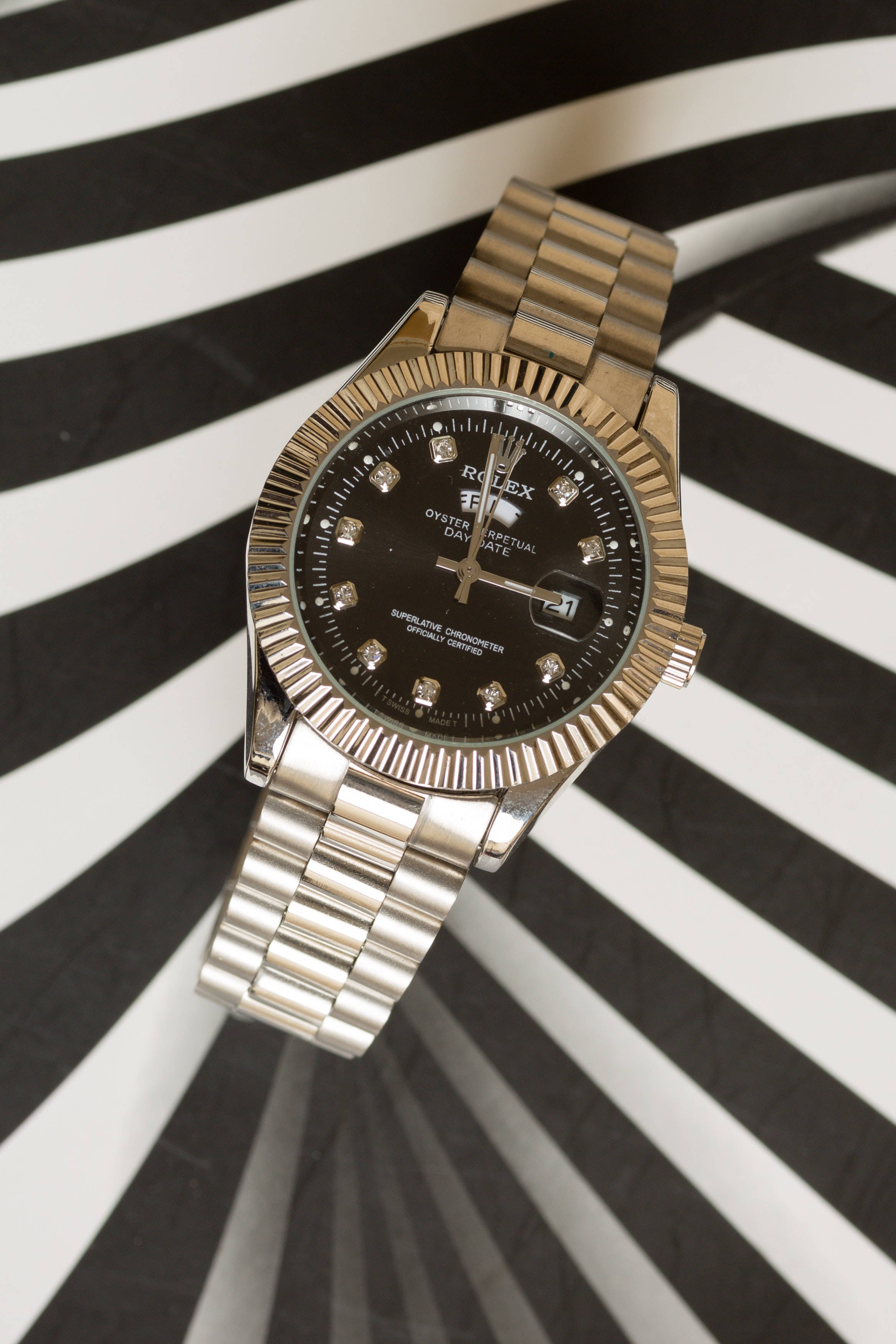 條紋勞力士 壁紙 — 一隻金色勞力士Oyster Perpetual Day-Date手錶，帶有鑽石時標，放置在醒目的黑白條紋背景上。