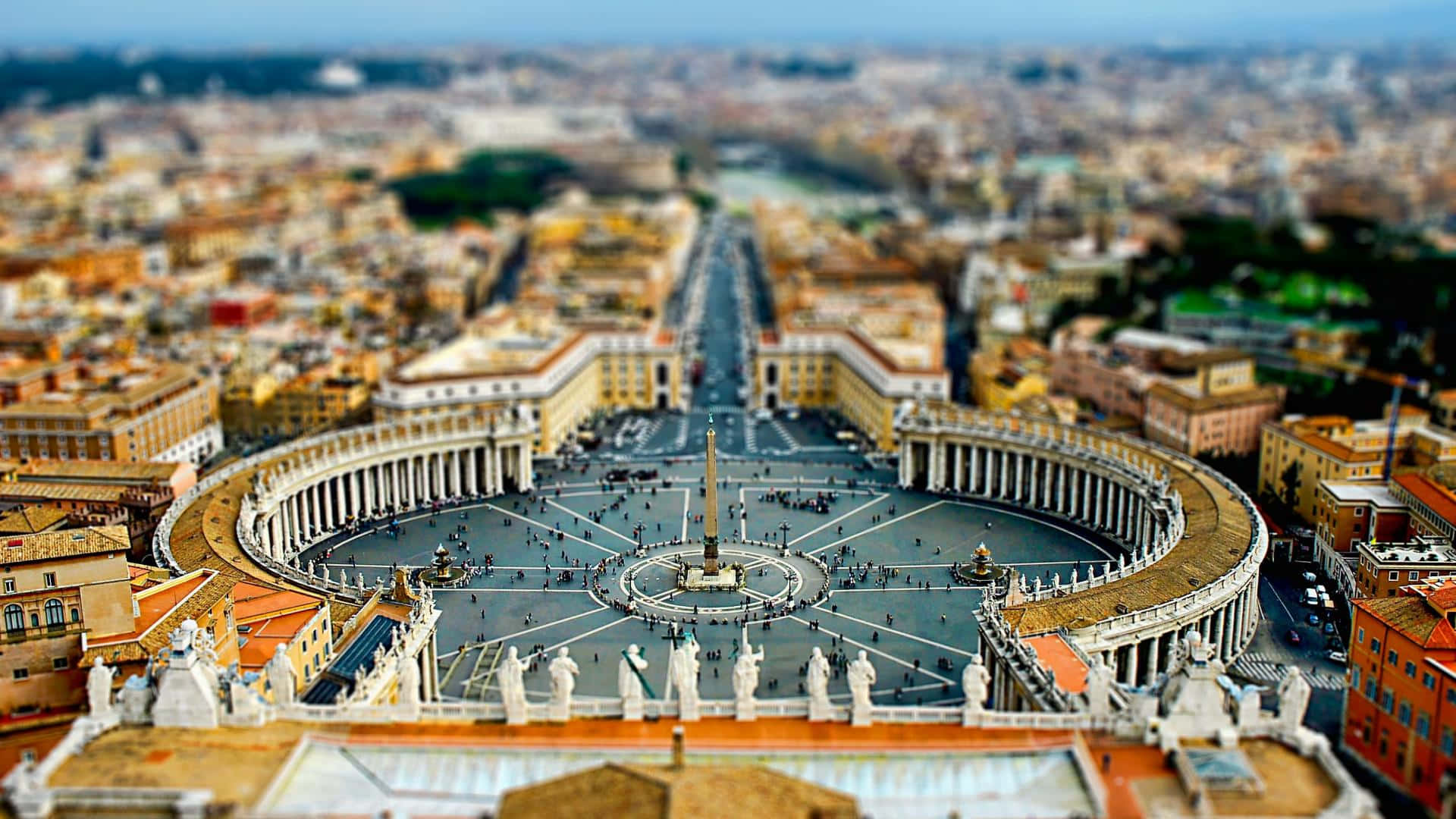 Rome 桌布 壁紙 — 梵蒂岡城聖彼得廣場的空中移軸攝影視角，模糊的城市景觀環繞著宏偉的柱廊和方尖碑。