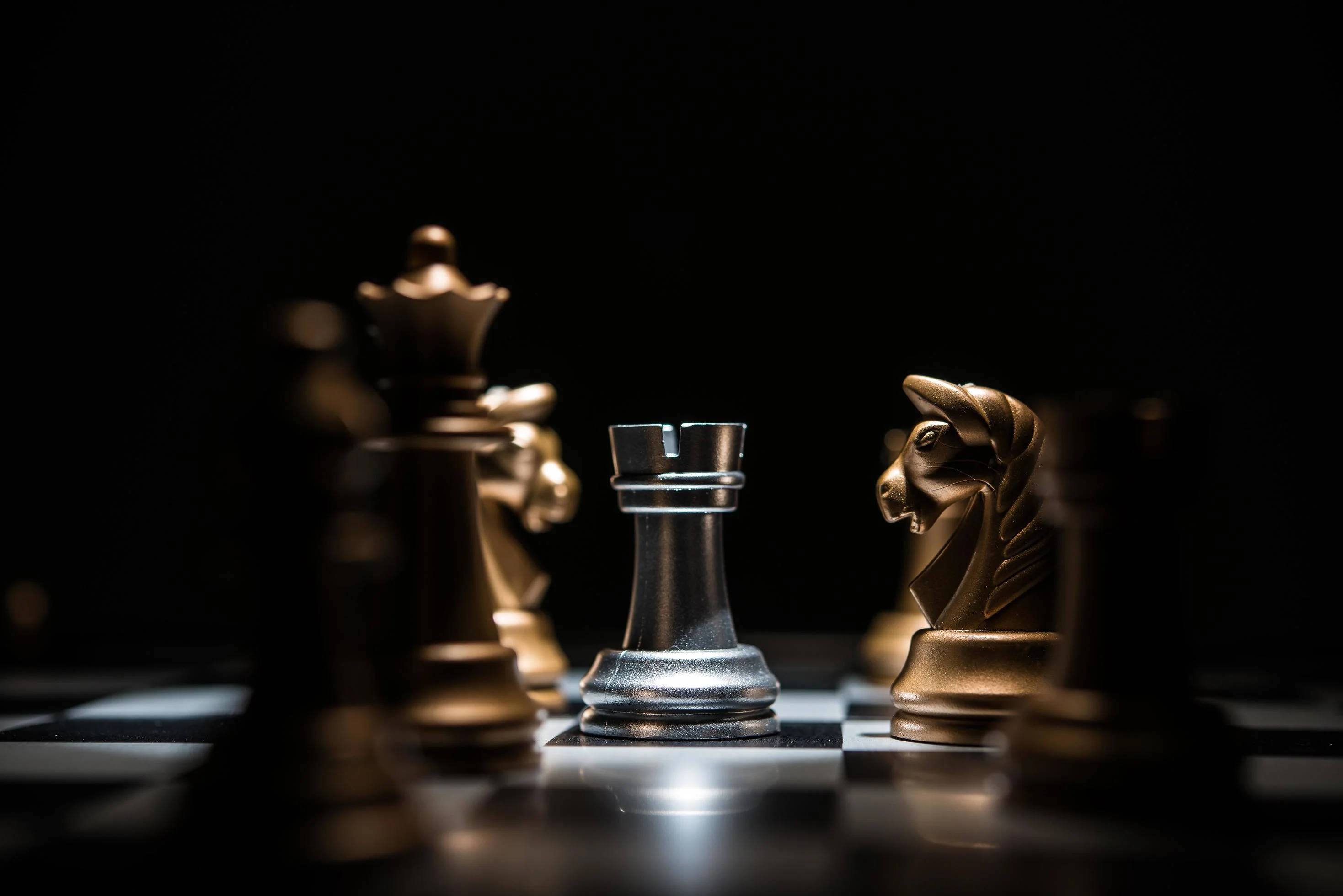 棋局 魔術師與騎士 壁紙 — 一個戲劇性的特寫，棋盤上的銀色城堡和金色騎士在聚焦燈光下對峙。