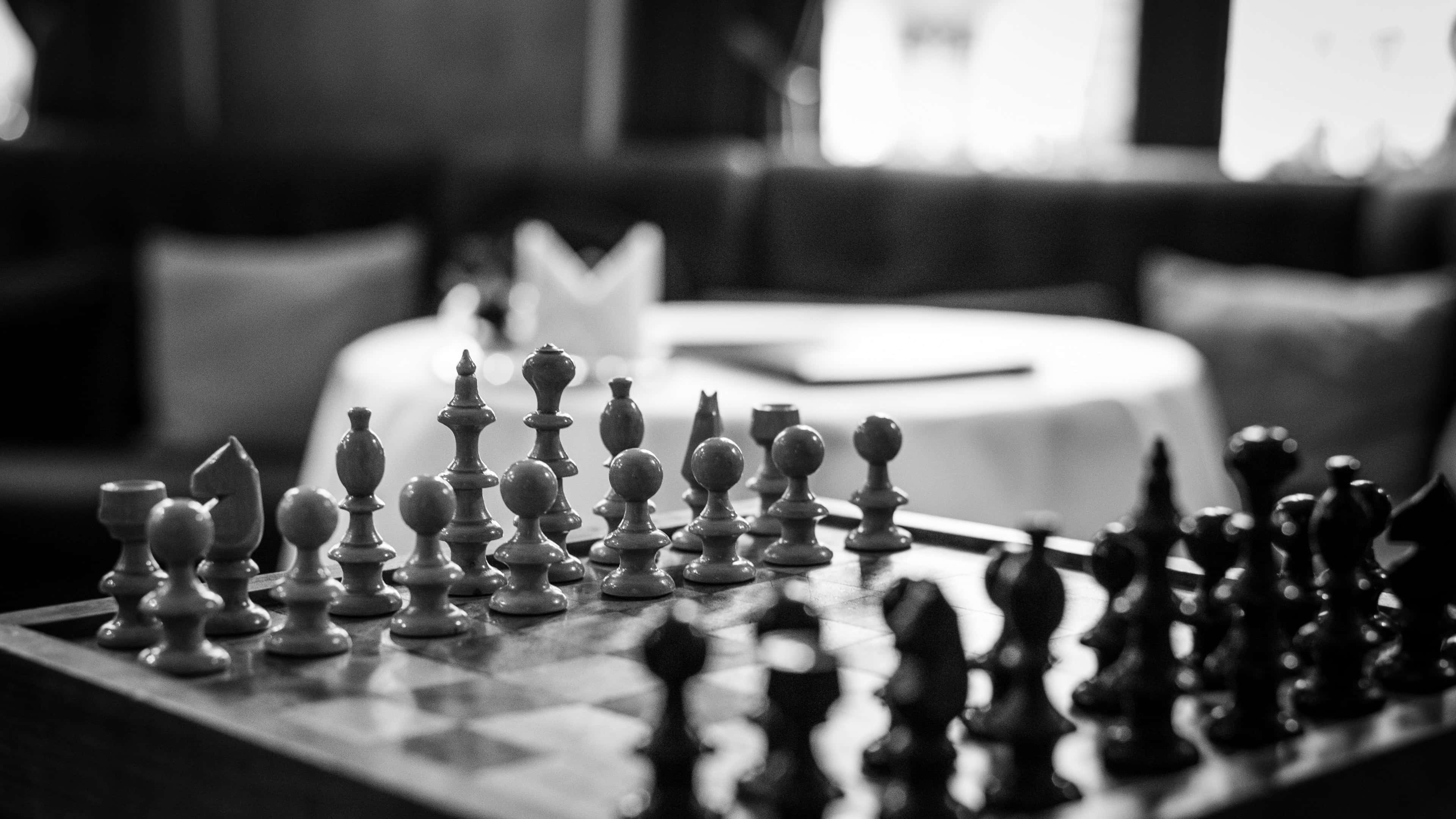 棋盤上的精妙棋局 壁紙 — 黑白特寫鏡頭，聚焦於棋盤上的棋子，背景是模糊的餐廳餐桌。
