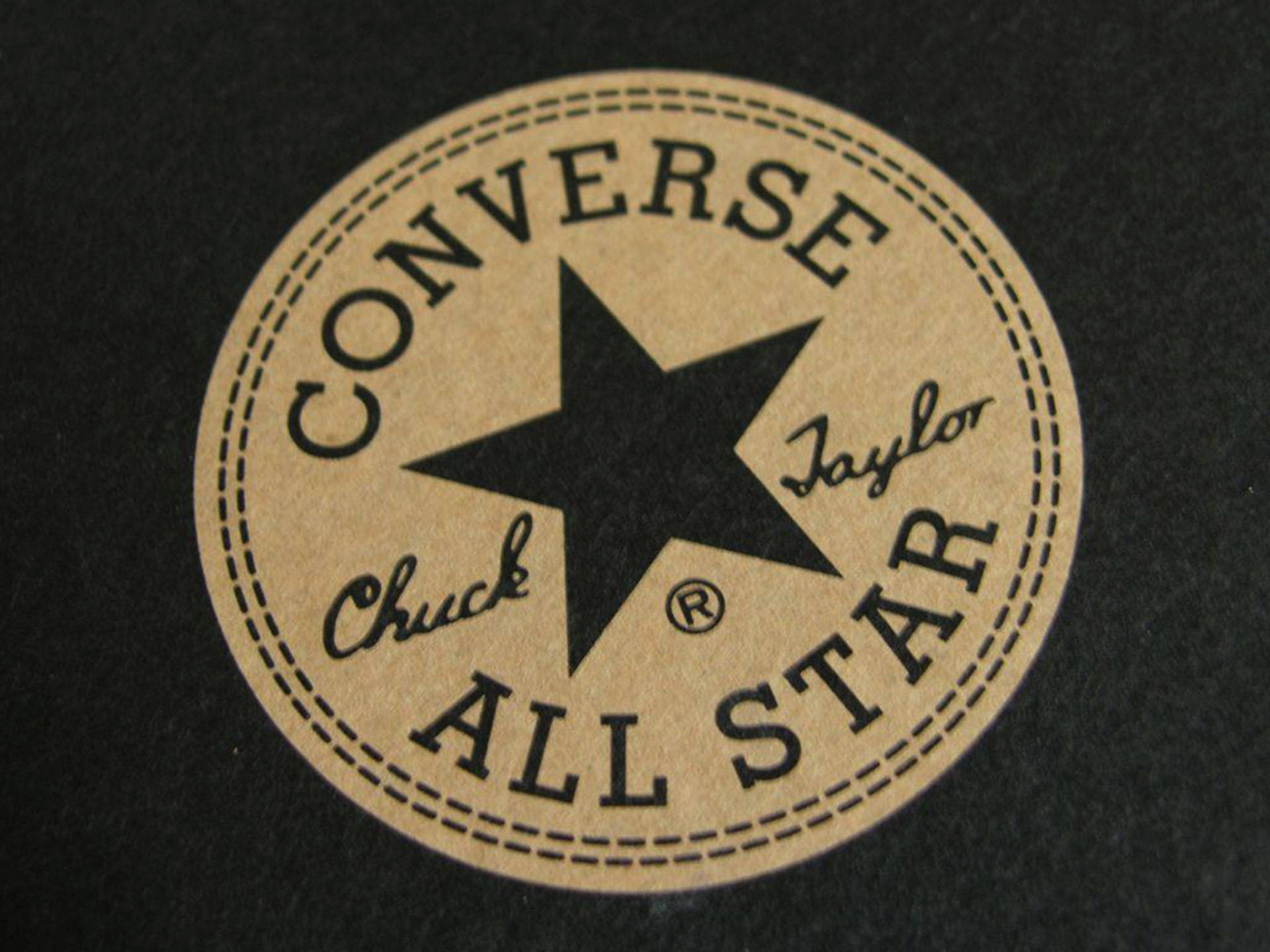 棕色 Converse 標誌 壁紙 — 經典 Converse Chuck Taylor All Star 標誌貼片在深色布料上的特寫，帶有縫合邊框。
