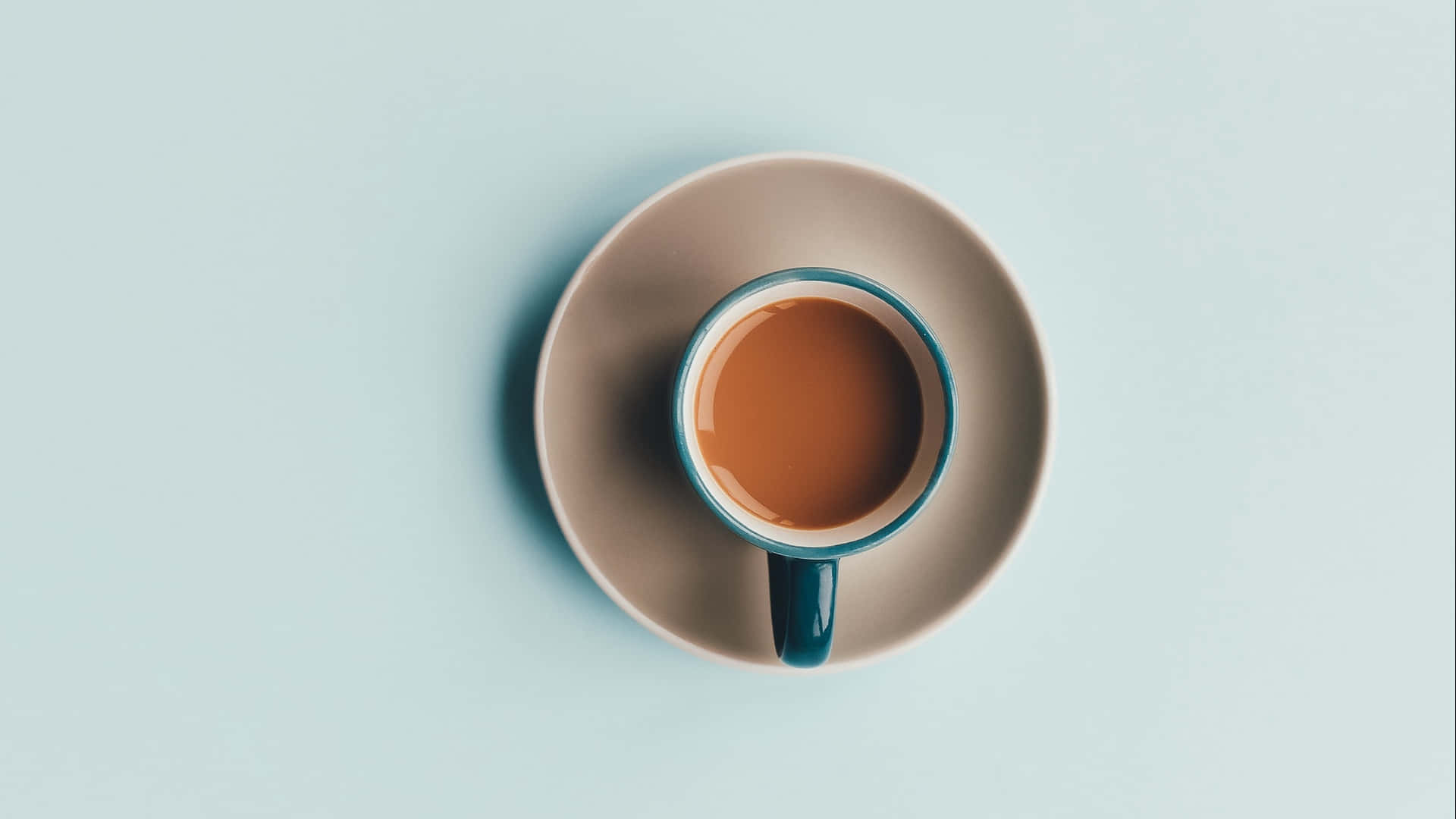 棕色咖啡杯圖片 壁紙 — 從上方俯瞰，一個帶有青綠色邊緣的咖啡杯放在米色碟子上，背景是柔和的藍色。