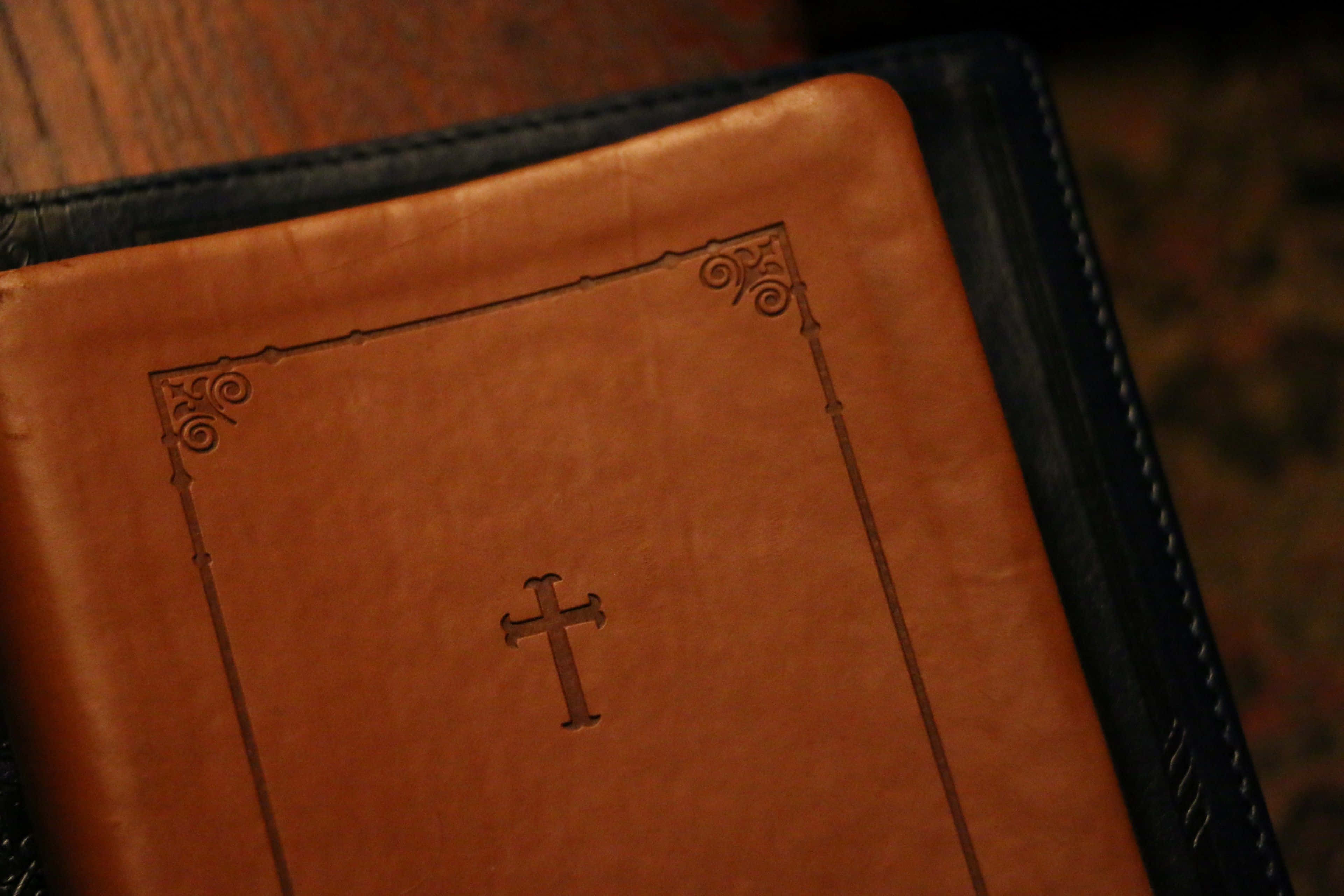 Bible Study 桌布 壁紙 — 棕色皮革聖經的特寫，帶有浮雕十字架和華麗邊框，放置在深色紋理表面上。