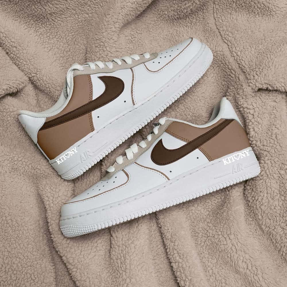 米色抓絨毯上的白色和棕色 Nike Air Force 1 運動鞋，帶有 'KITONY' 品牌標誌。