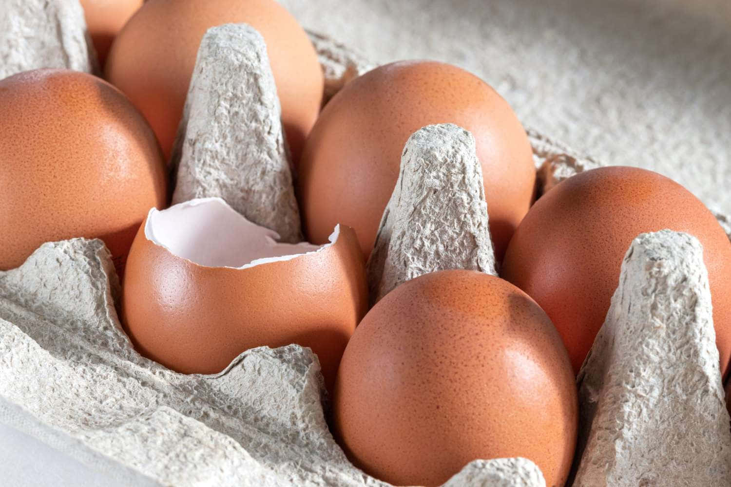 Eggshell 桌布 壁紙 — 棕色雞蛋在紙板托盤中的特寫，其中一個破裂露出白色內部。