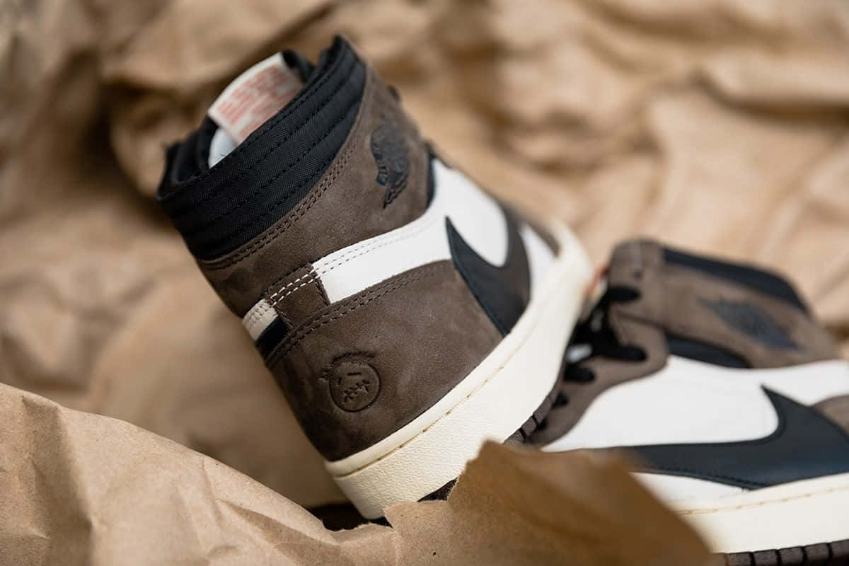 Travis Scott Jordan 1 桌布 壁紙 — 棕色麂皮高筒運動鞋的特寫，帶有黑色和白色點綴，放在皺巴巴的棕色紙上。