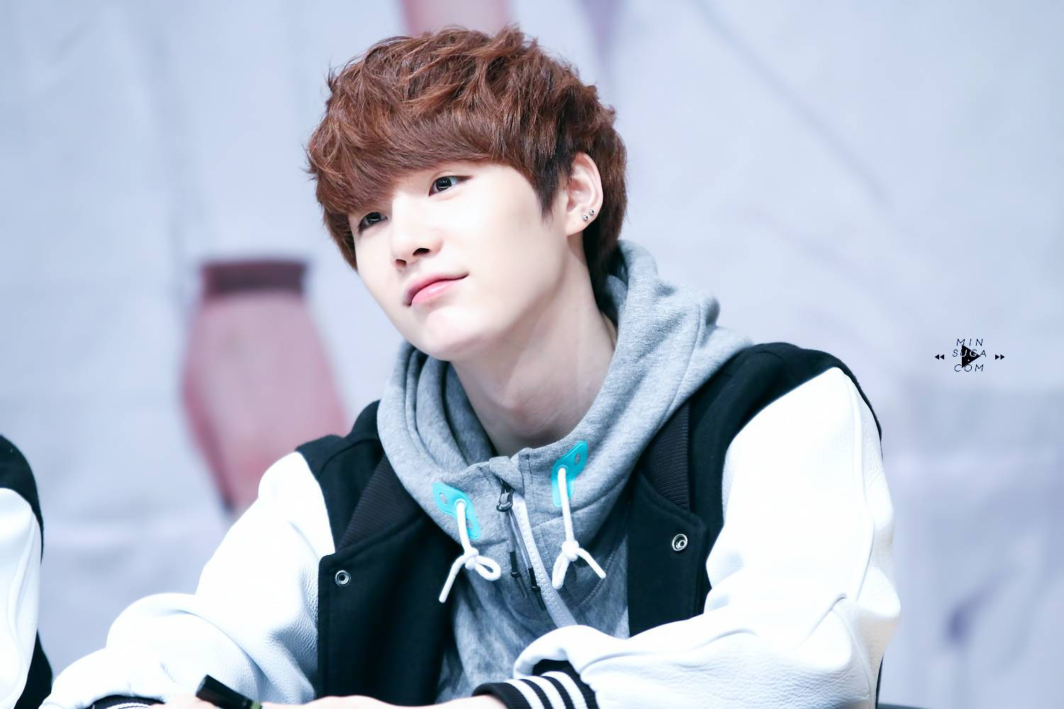 棕髮 BTS Suga 壁紙 — 一位紅棕色頭髮的年輕男子穿著灰色連帽衫，外搭黑白夾克，若有所思地向上看。