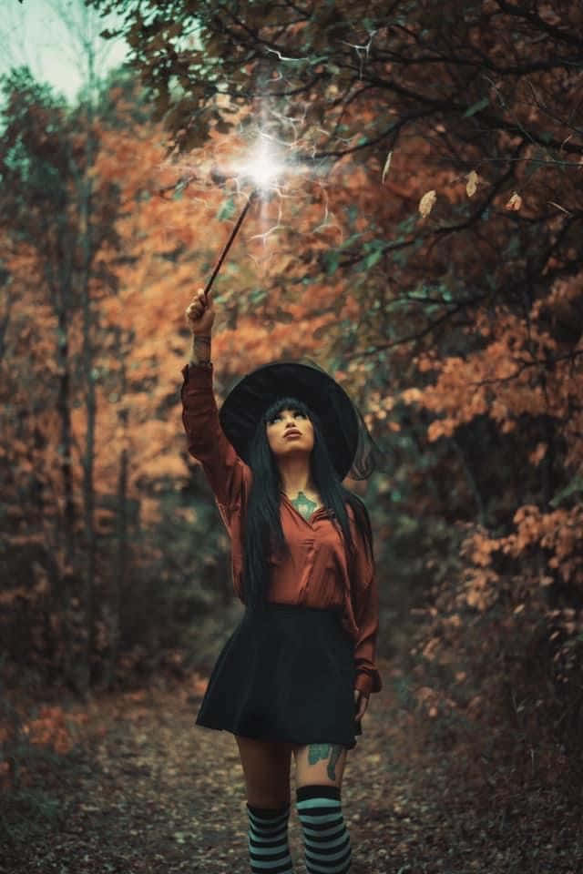 Witch Costumes 桌布 壁紙 — 森林中的年輕女巫手持發光的魔杖，在秋葉間灑出火花。