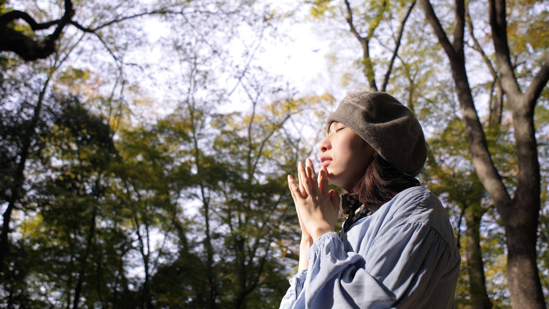 戴冷帽的年輕女性在秋樹下冥想，陽光穿過樹葉灑落。
