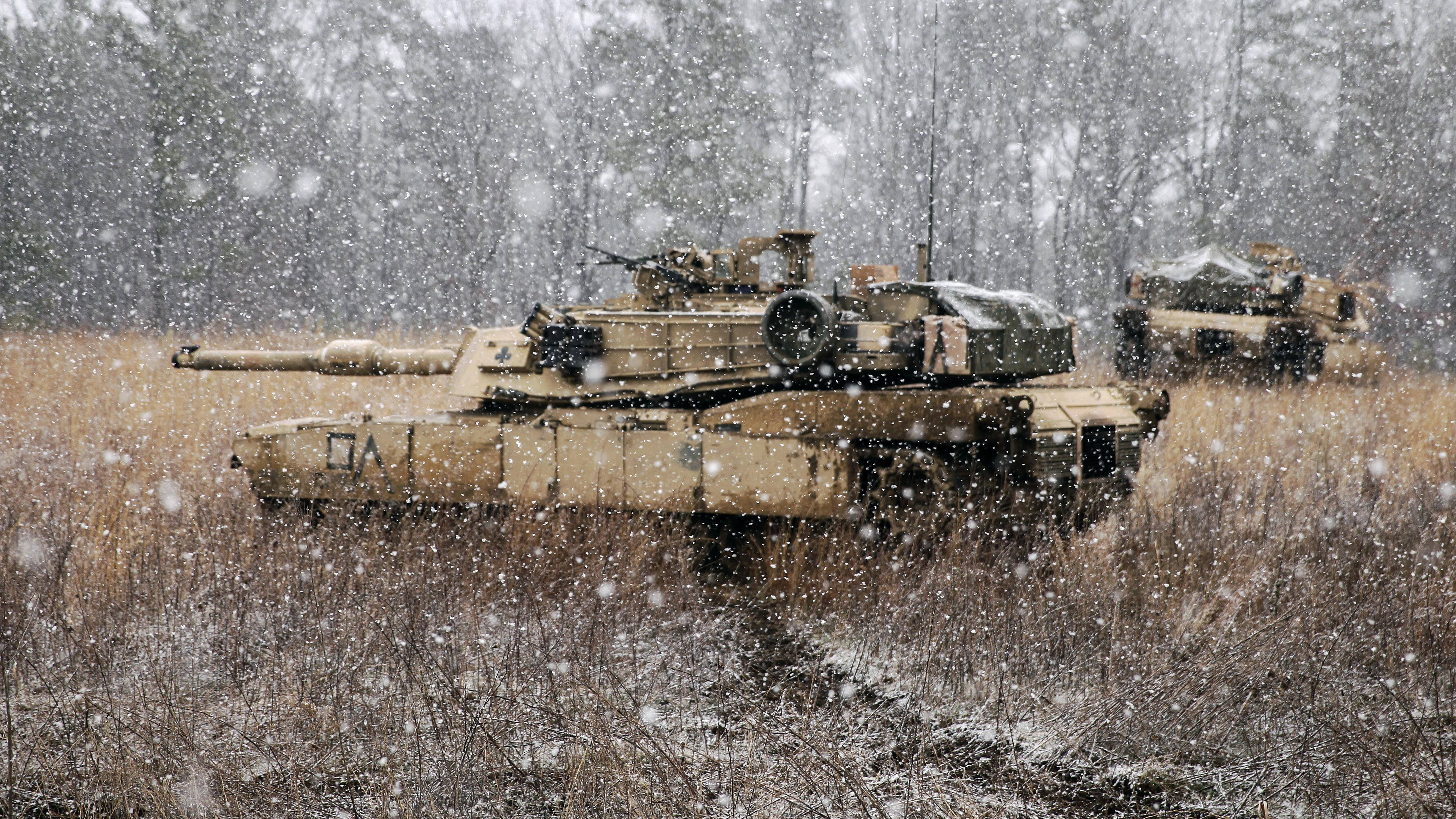 森林中的軍隊坦克 壁紙 — 兩輛軍用坦克靜止在雪地上，背後有光禿禿的樹木，大雪紛飛。