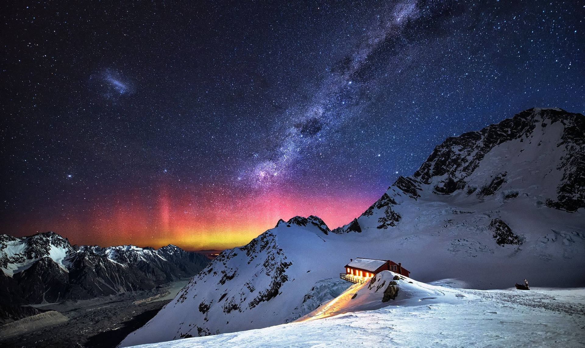 在星空和北極光下，白雪覆蓋的山上發光的小屋。