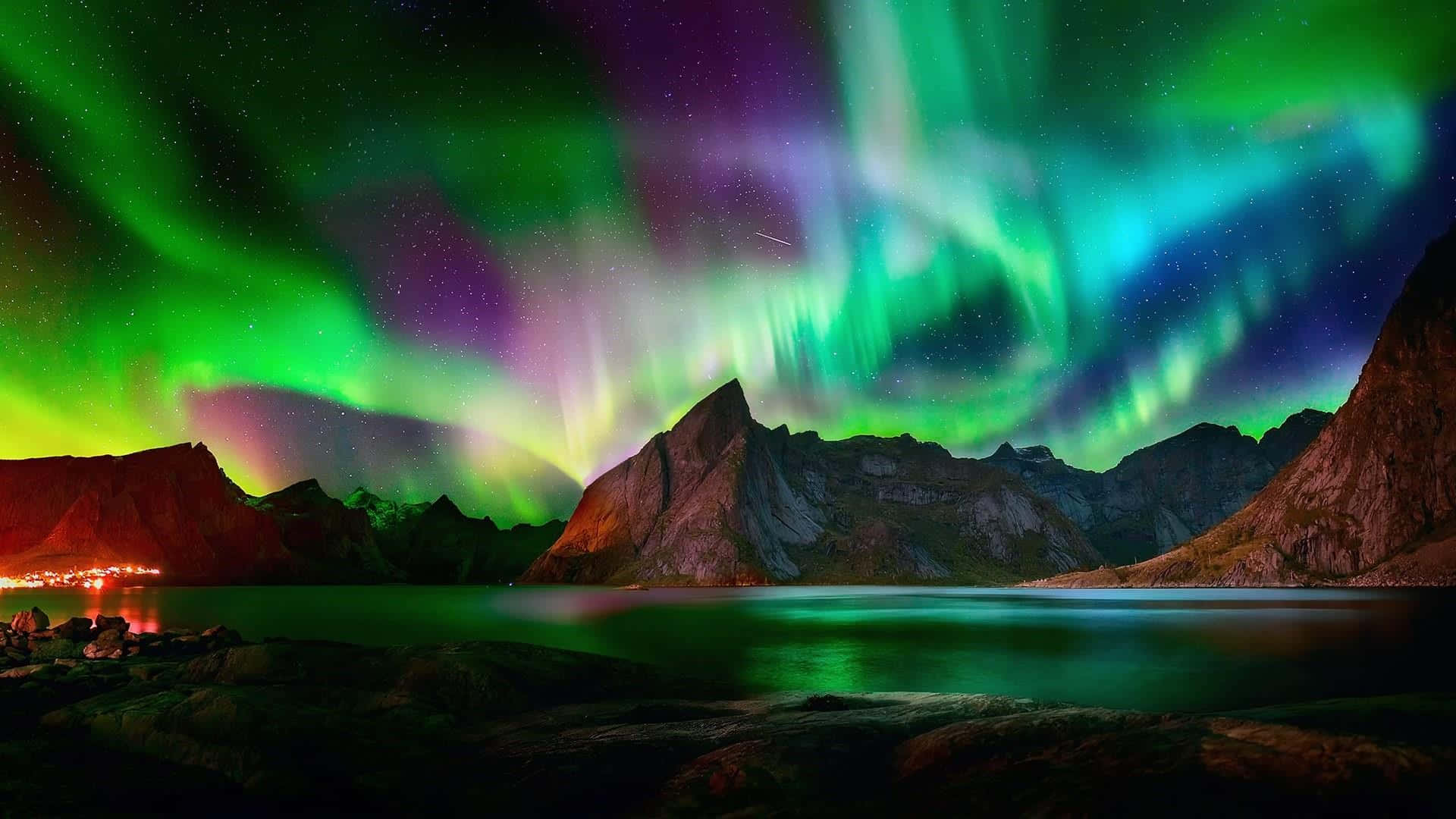 極光以迷人的光暈裝點夜空 壁紙 — 鮮豔的綠色和紫色極光在星夜下平靜的湖面上倒映的鋸齒狀山脈上方舞動。
