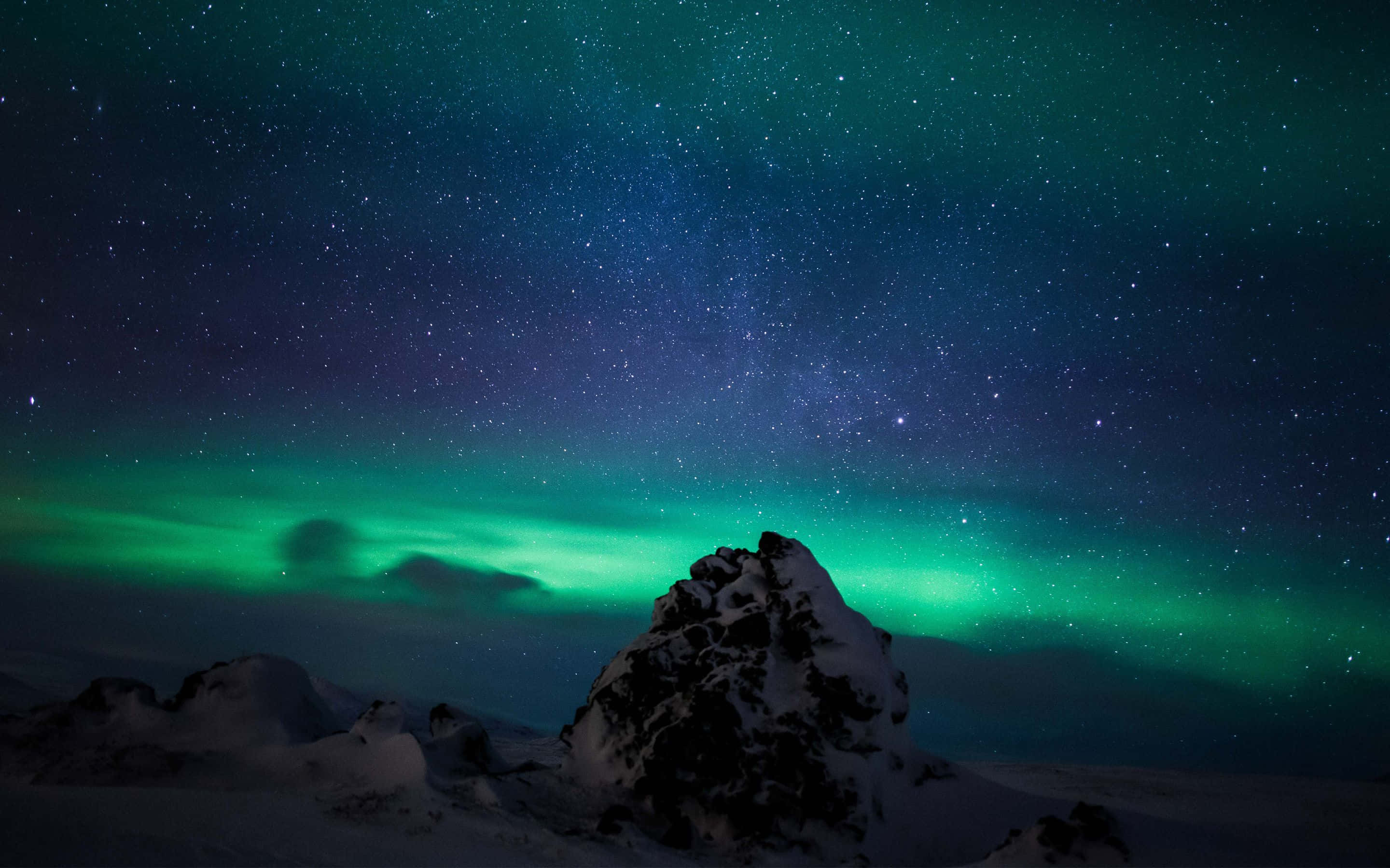 極光在夜空中綻放，如萬花筒般絢麗 壁紙 — 一座積雪的山峰矗立在充滿活力的綠色北極光下，北極光在繁星點點的夜空中舞動。
