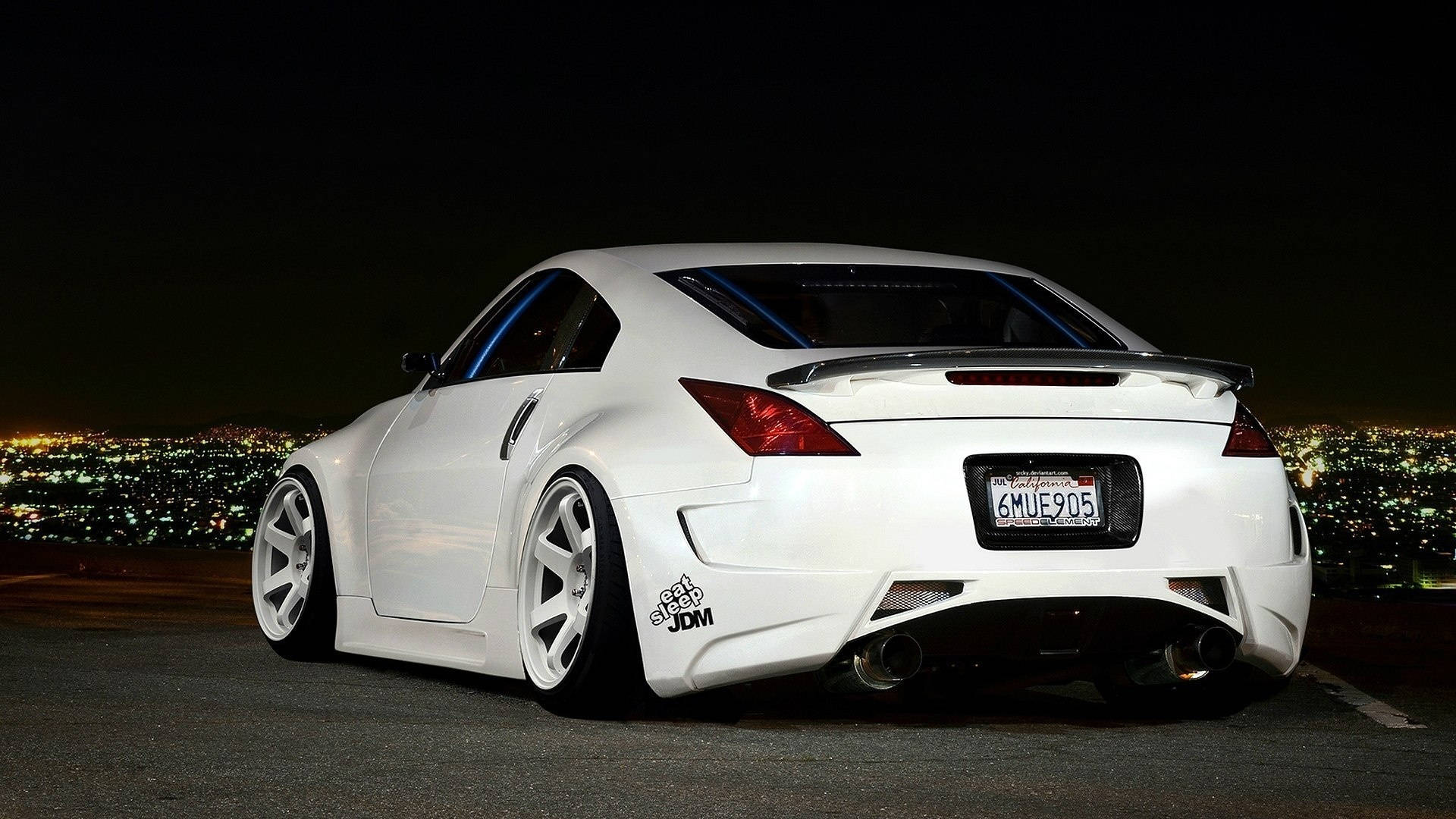 極具運動感的 Nissan 350Z 壁紙 — 一輛白色改裝跑車配備定制輪轂和雙排氣管，在夜間停泊，俯瞰著閃爍的城市景觀。