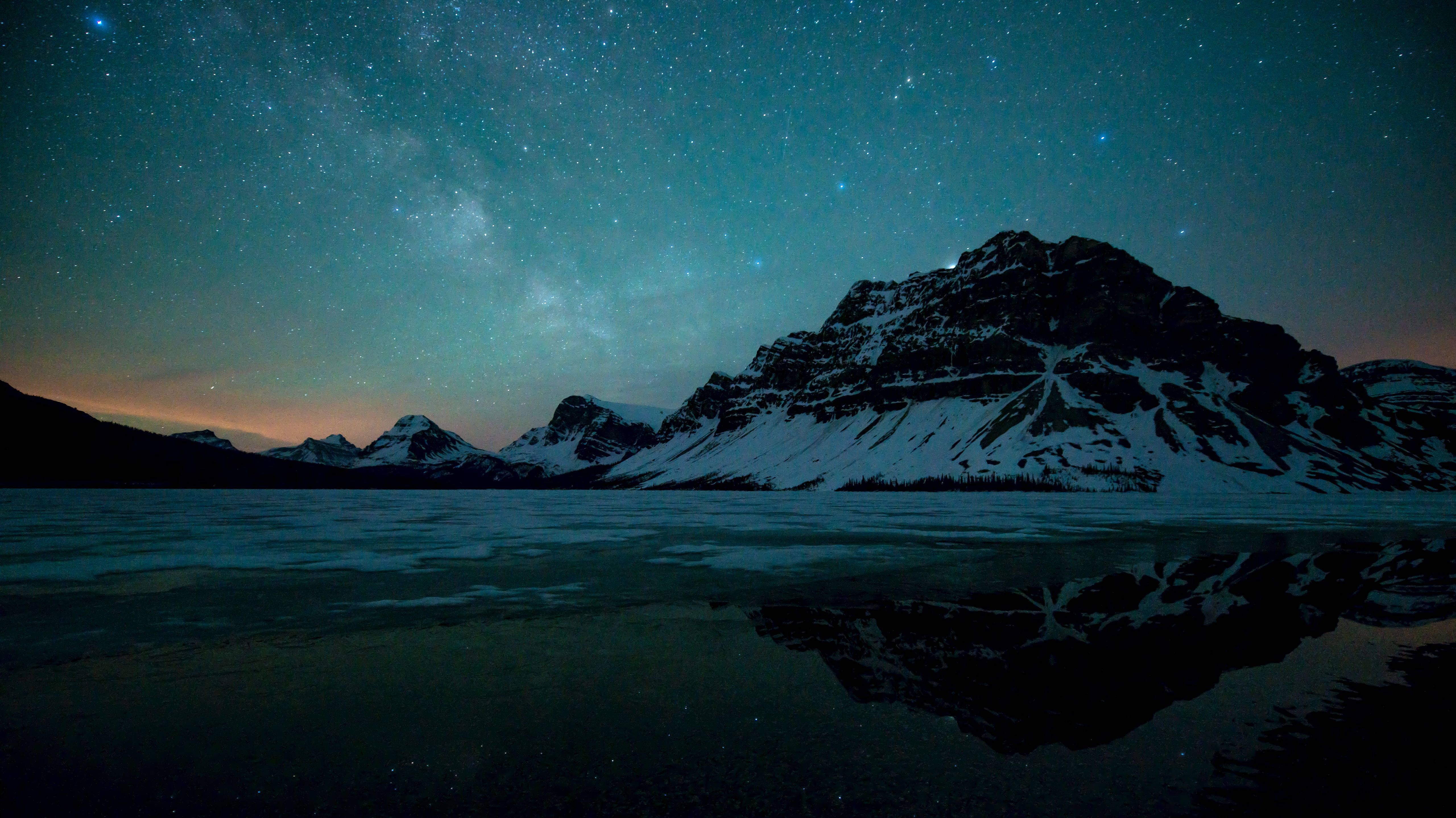 極地雪山 MacBook Pro 4K 壁紙 — 積雪的山峰在繁星點點的夜空下倒映，銀河在冰凍的湖面上拱起。