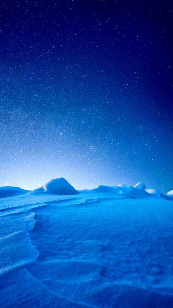 極地風景 iPhone 活動壁紙 壁紙 — 星空籠罩著寧靜的雪景，帶有柔和的藍色調和溫和起伏的地形。