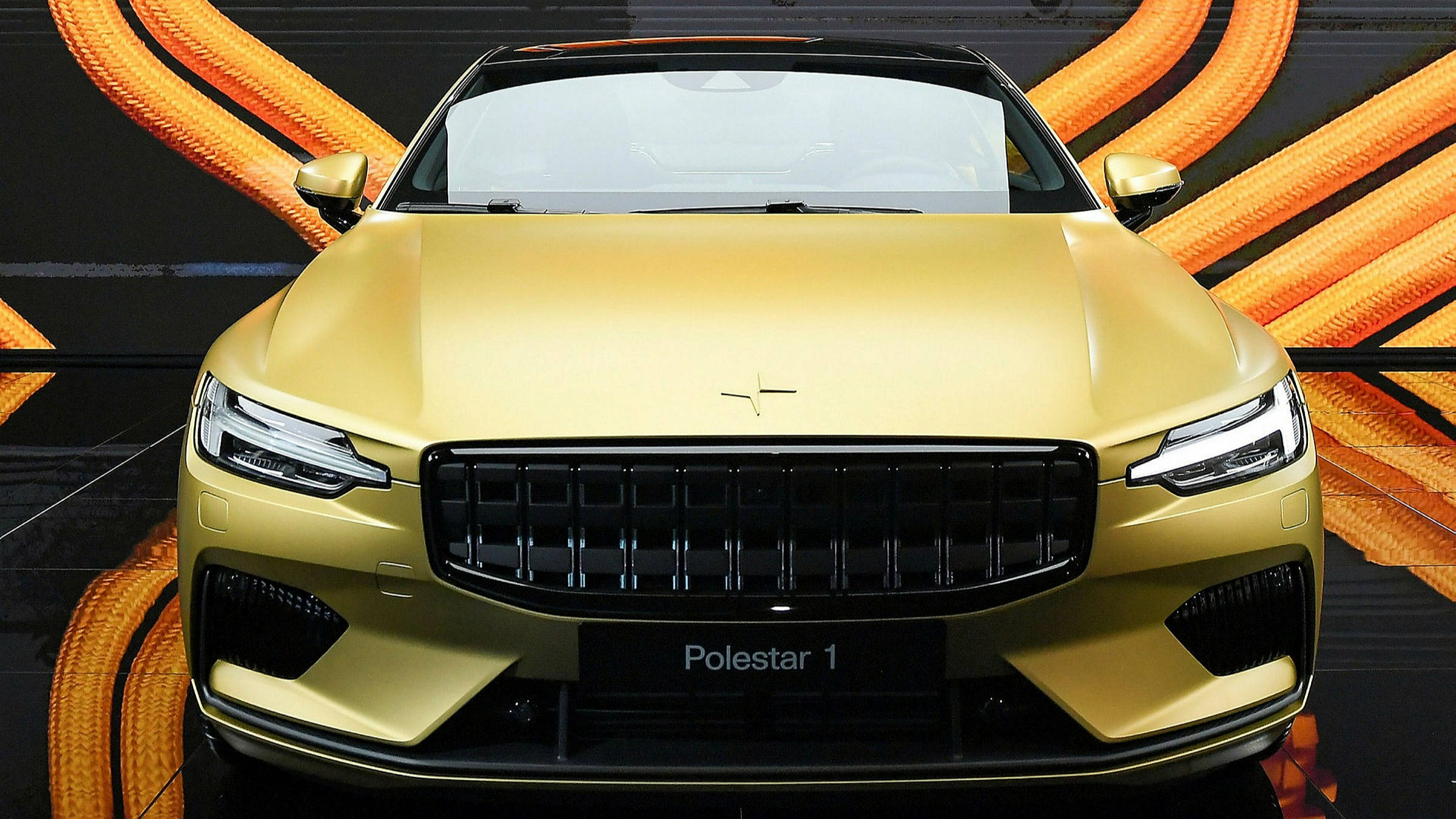 極星1特別版 壁紙 — 閃亮的金色Polestar 1跑車在工作室環境中，以動態的橙色電纜背景展示。