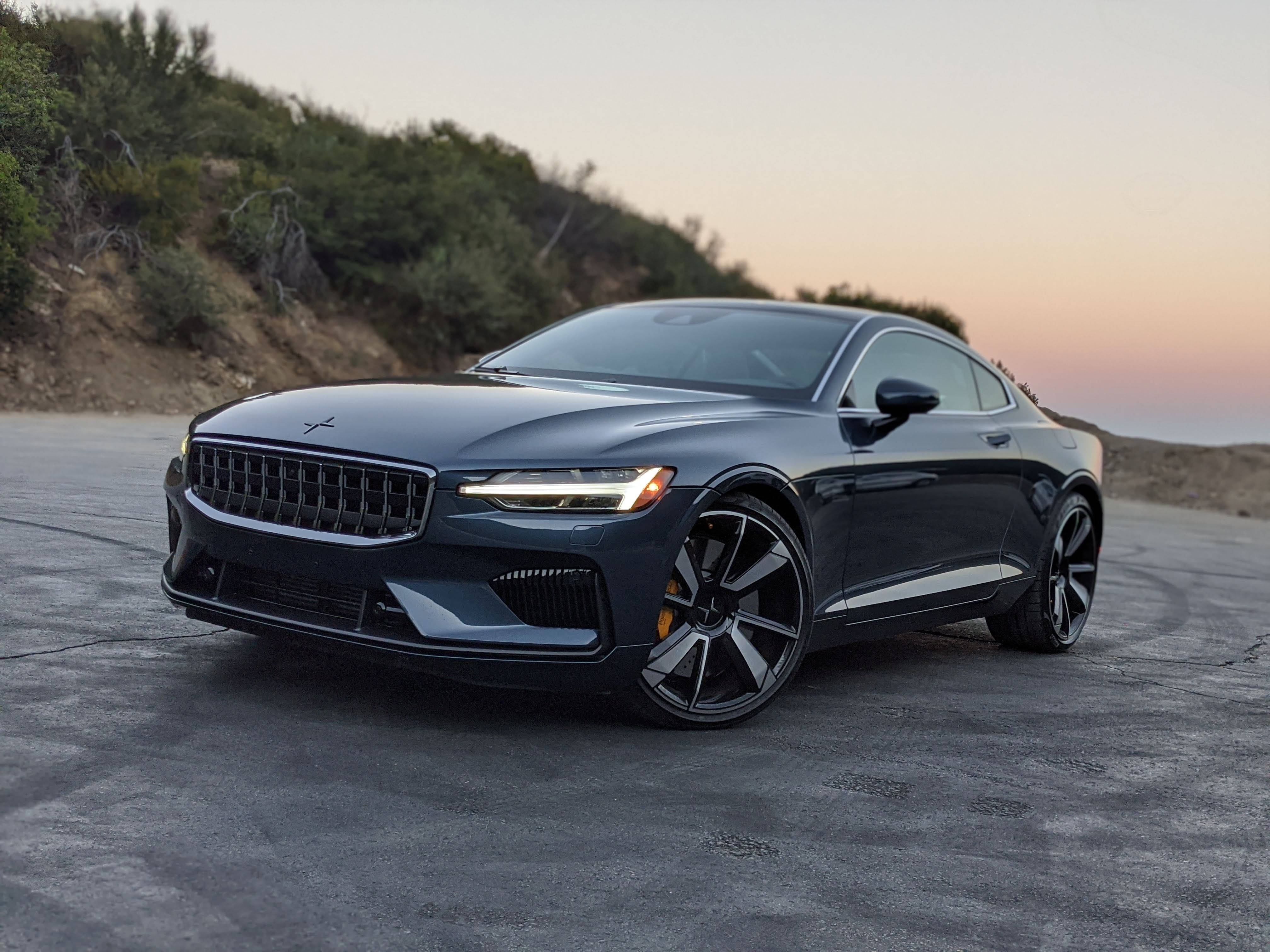 極星運動車 壁紙 — 一輛時尚的深灰色Polestar 2電動轎跑車停在日落時分的混凝土道路上，背景有山丘。
