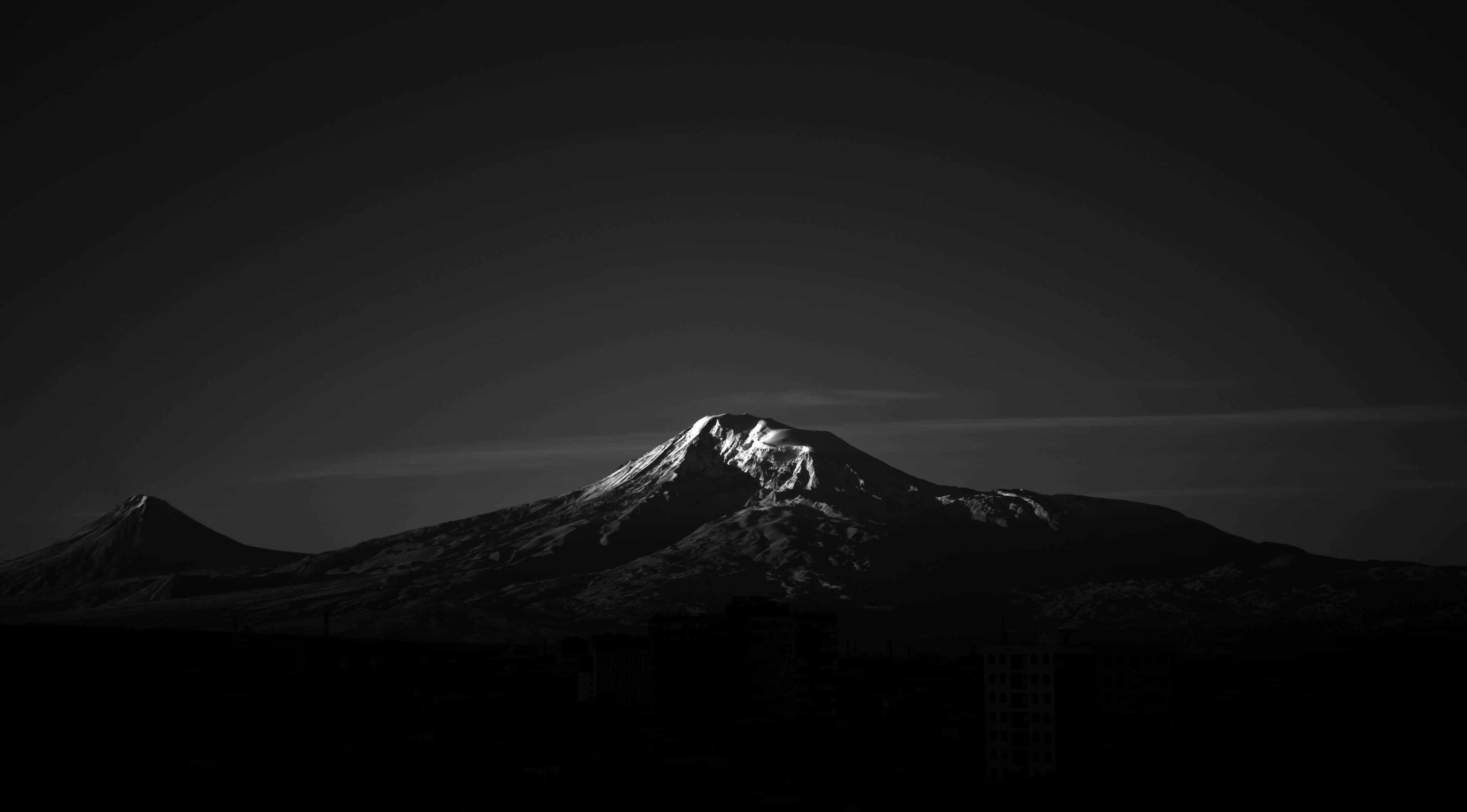 極簡主義者的夢想 — 純黑背景 壁紙 — 一座黑白分明的山峰，頂部積雪，在漸變天空下聳立於剪影城市景觀之上。