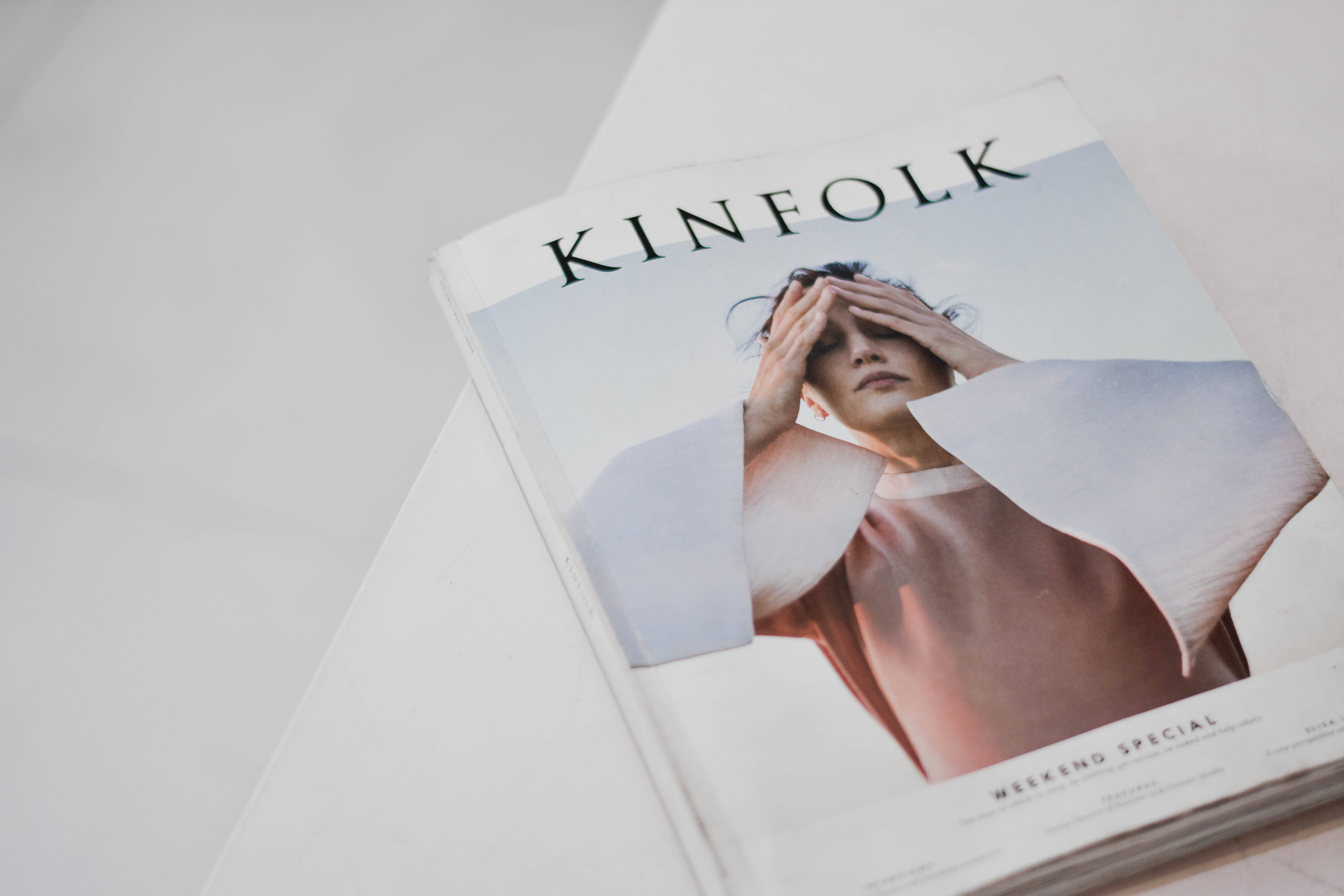 極簡封面雜誌 壁紙 — 一本名為 'KINFOLK' 的雜誌，封面有女性遮住眼睛，放在白色表面上。