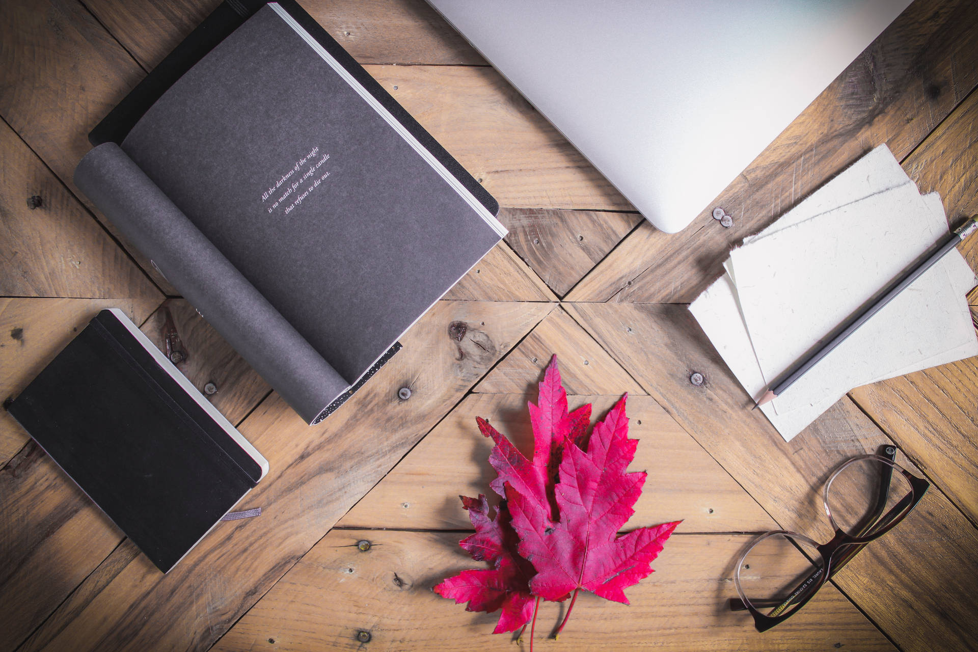 木製書桌上有手提電腦、筆記本、眼鏡和一片紅楓葉。